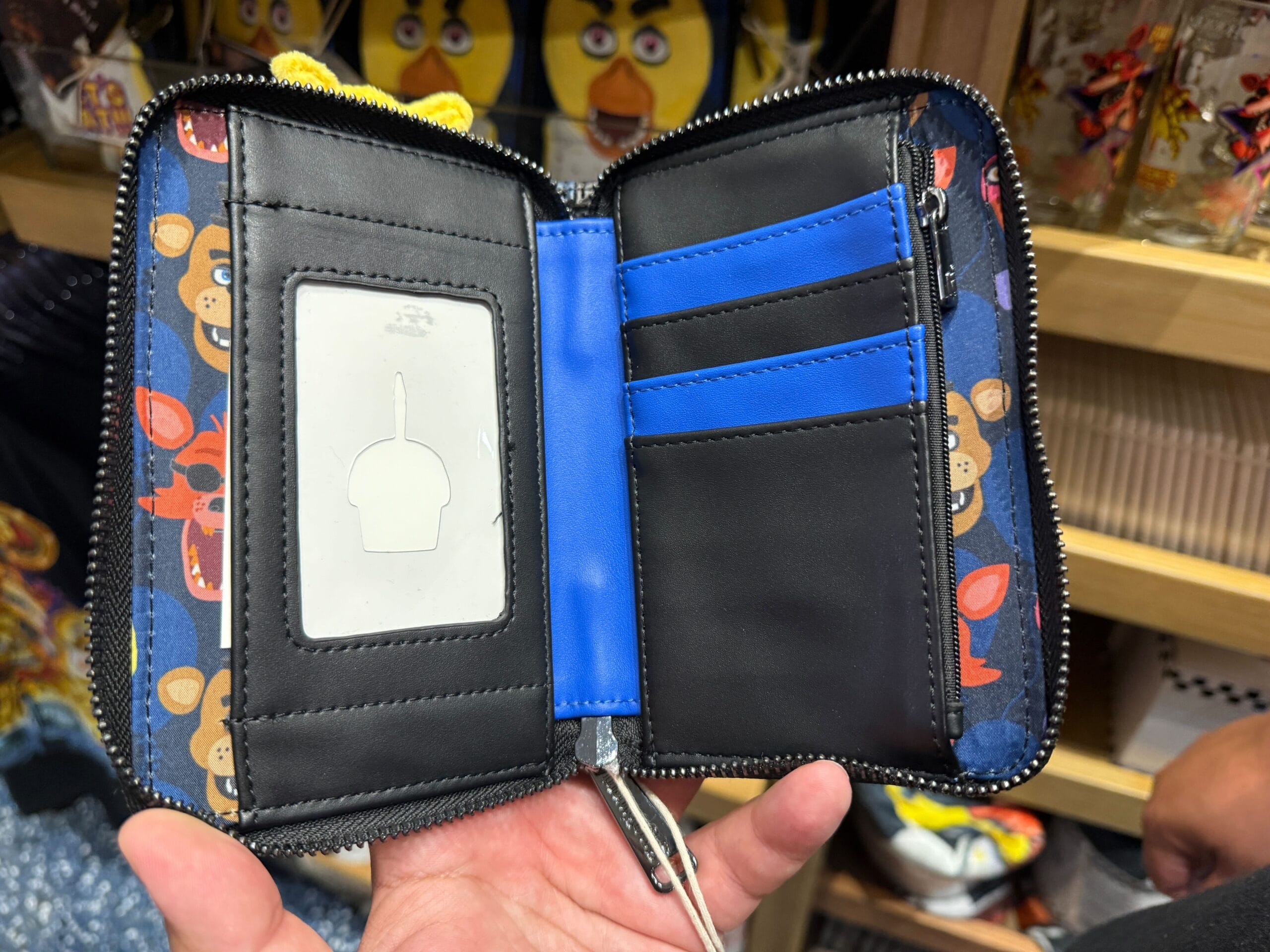 A hand holds an open Loungefly wallet with cartoon bear faces and blue card slots, displayed in a store.
