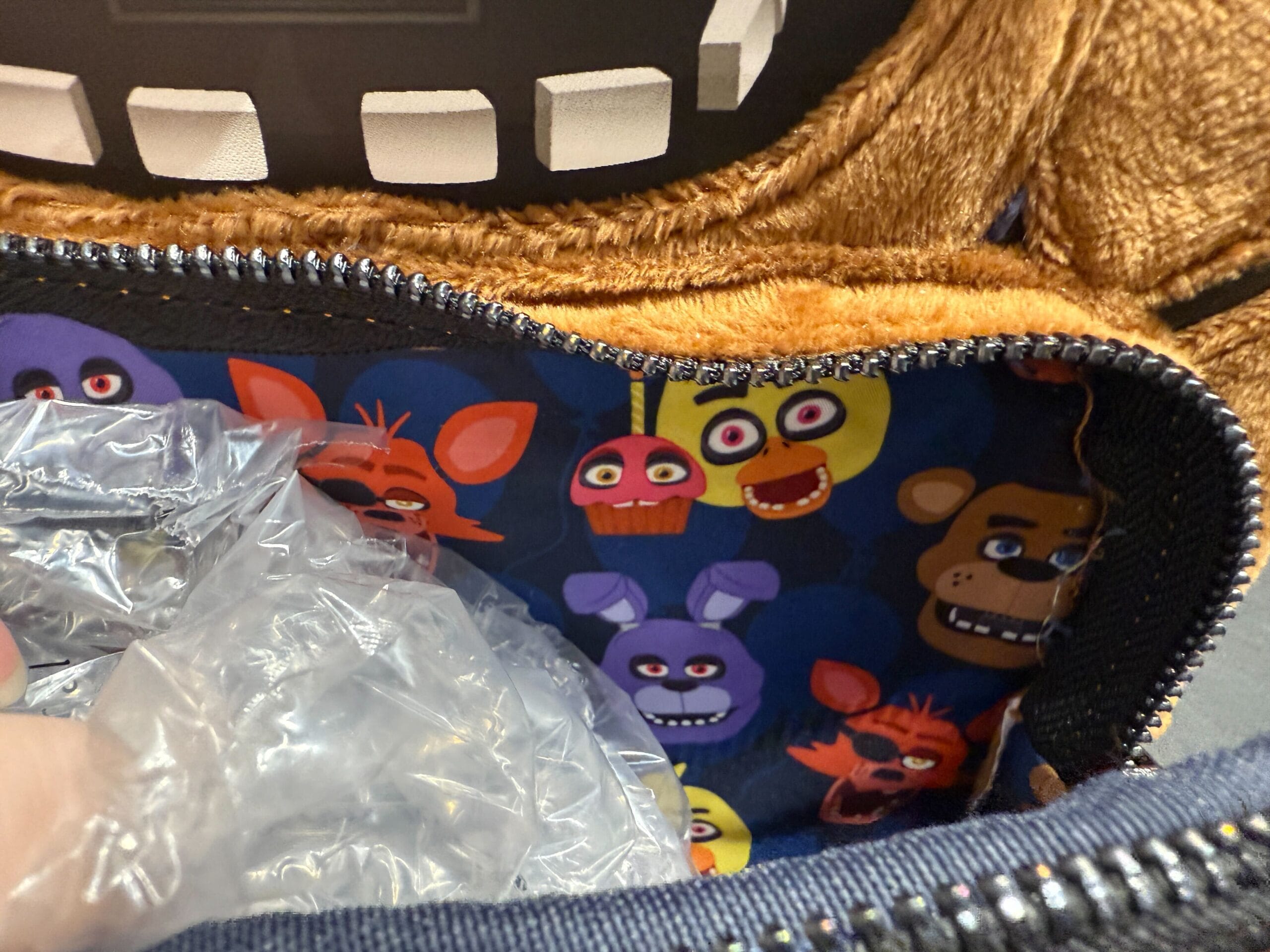 Inside a zippered Loungefly bag with cartoon animal faces and a hand holding bubble wrap.