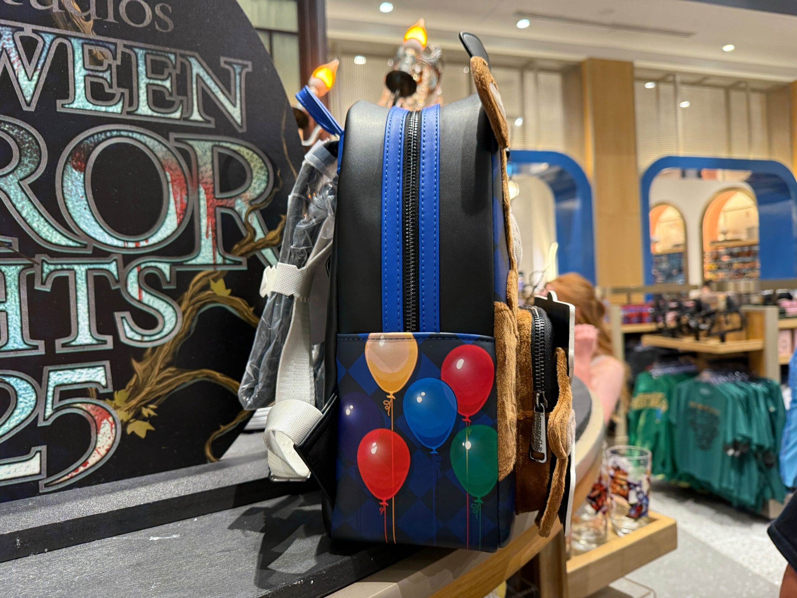 A Loungefly backpack with colorful balloons is displayed in a store near Halloween-themed merchandise.