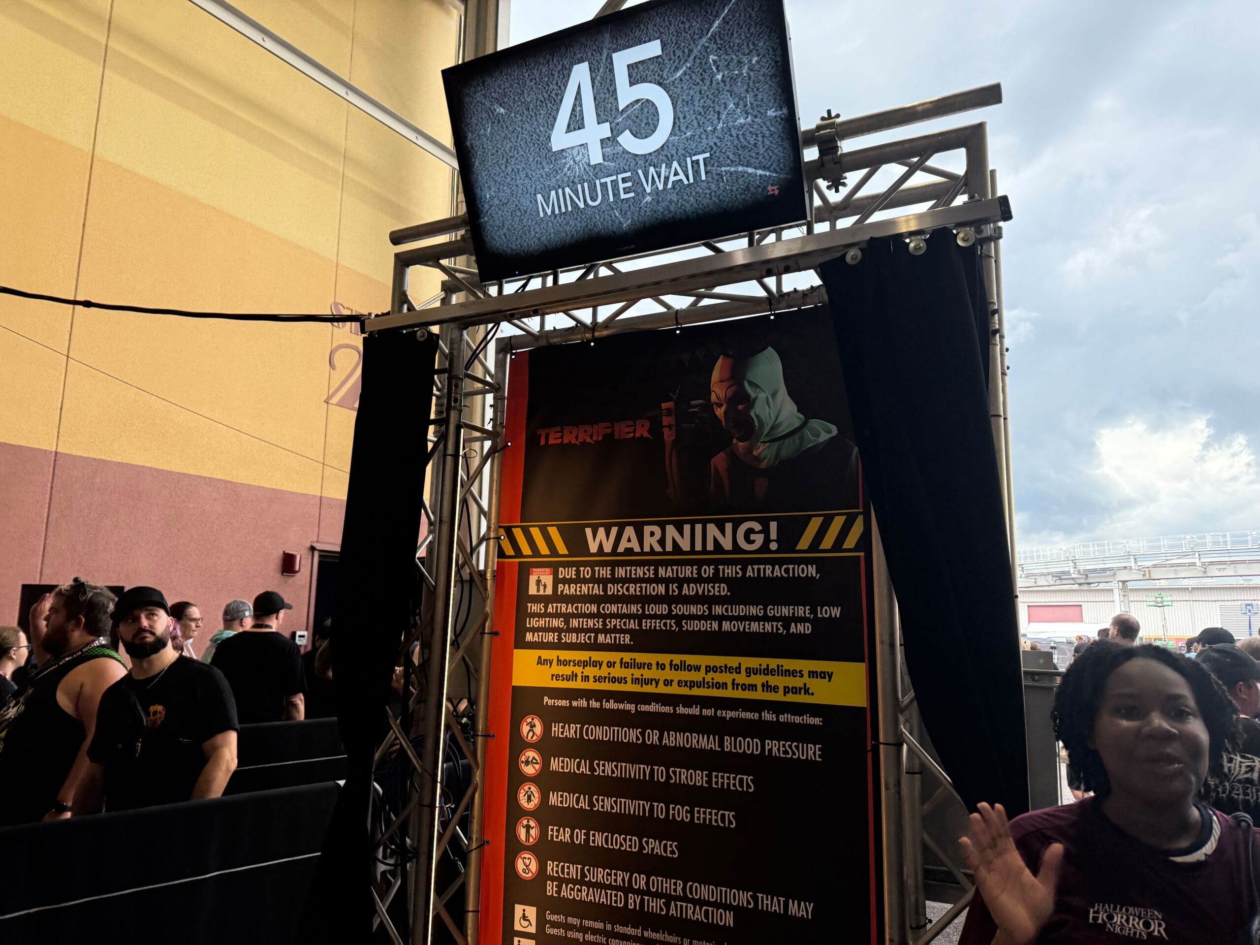 Indoor queue area with a "45 Minute Wait" sign for a Halloween Horror Nights attraction; guests wait in line.