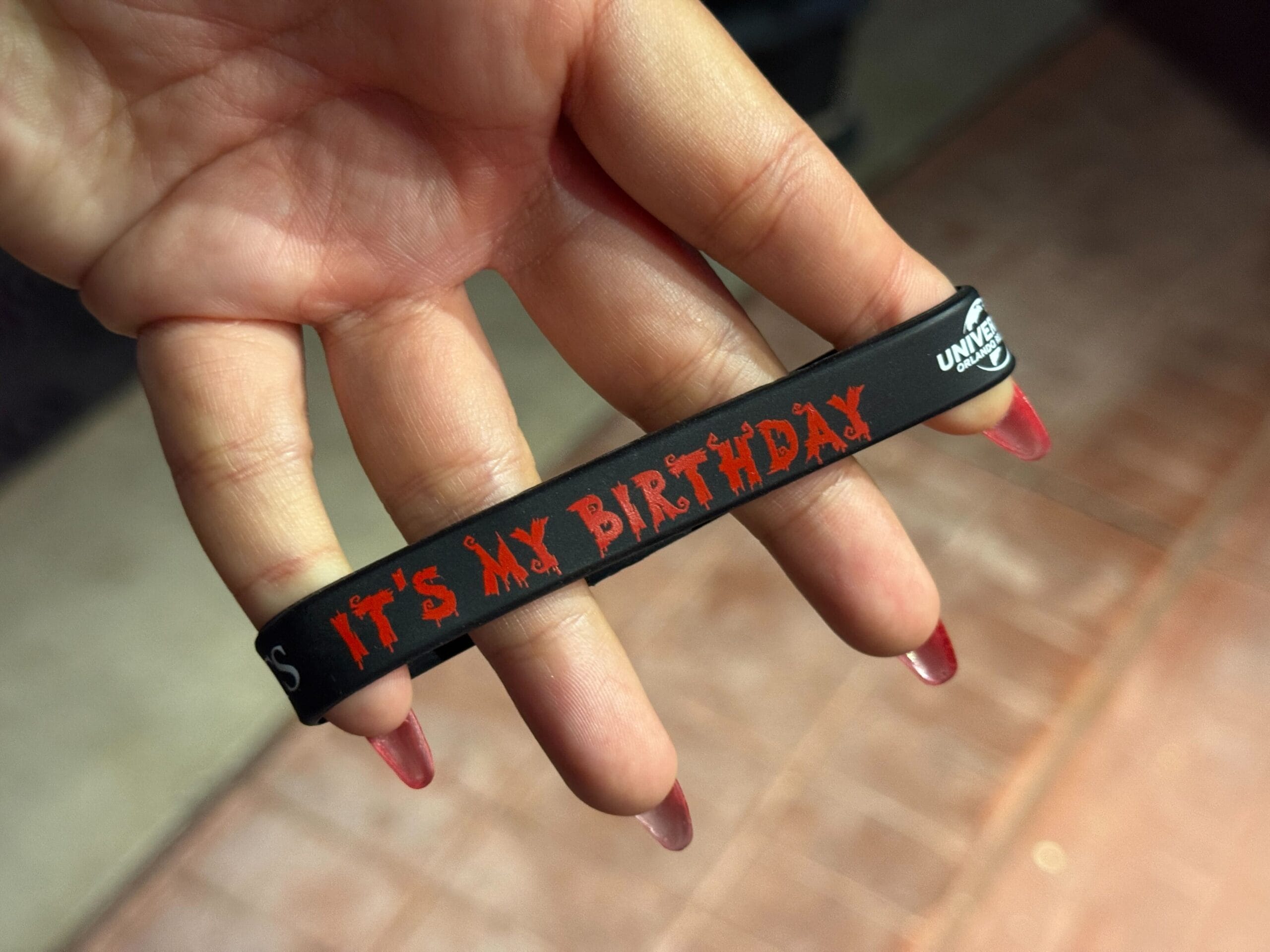 A hand holding a black Birthday Wristband with red text that reads "IT'S MY BIRTHDAY" at HHN.