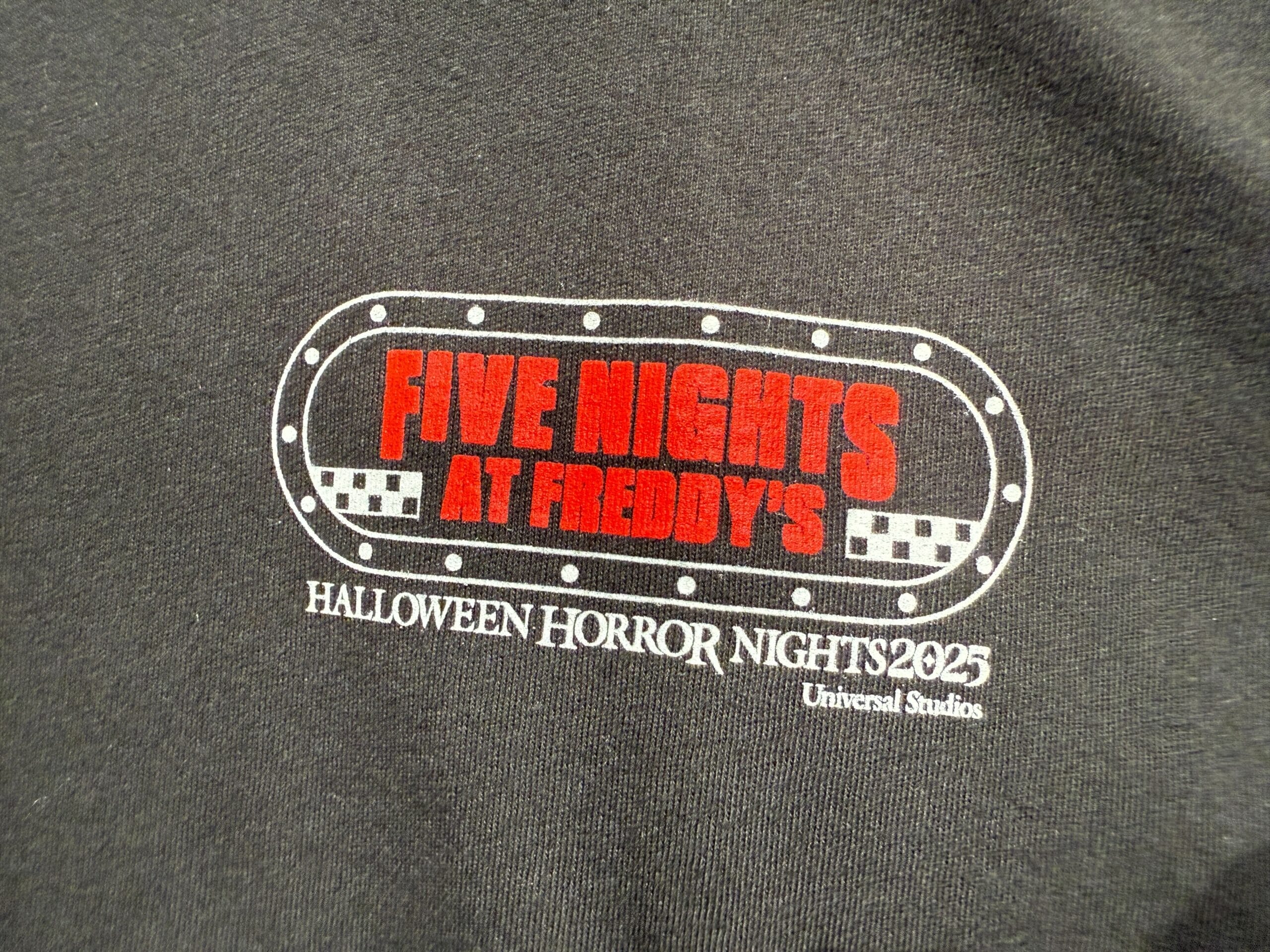 Black shirt with "Five Nights at Freddy's" and "Halloween Horror Nights 2025 Universal Studios" printed on it.