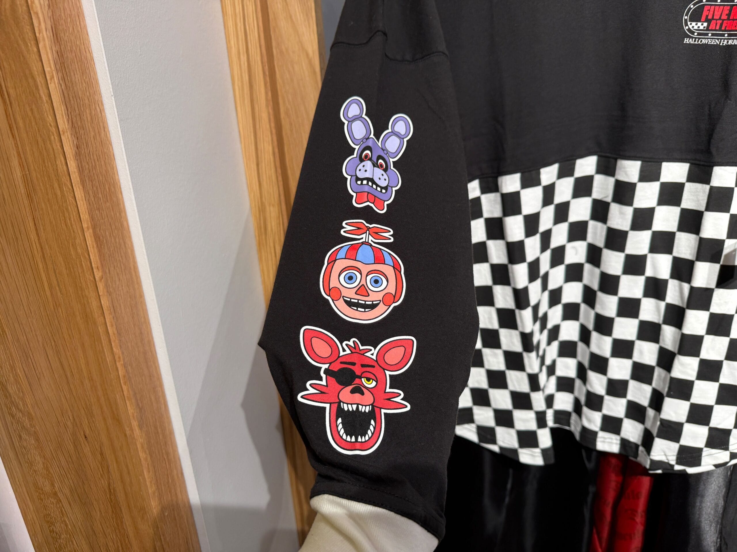 Three cartoon faces from Five Nights at Freddy’s are printed on a black sleeve with a black-and-white checker pattern.