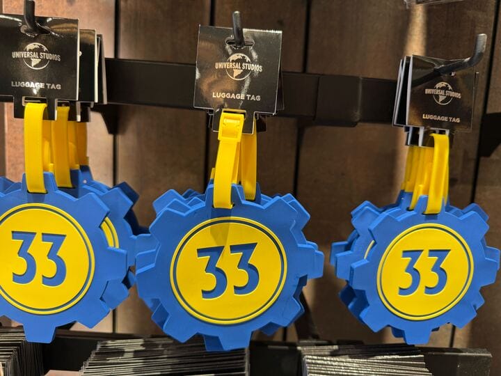 Three blue and yellow luggage tags shaped like gears, each with the number 33, hanging on display hooks.