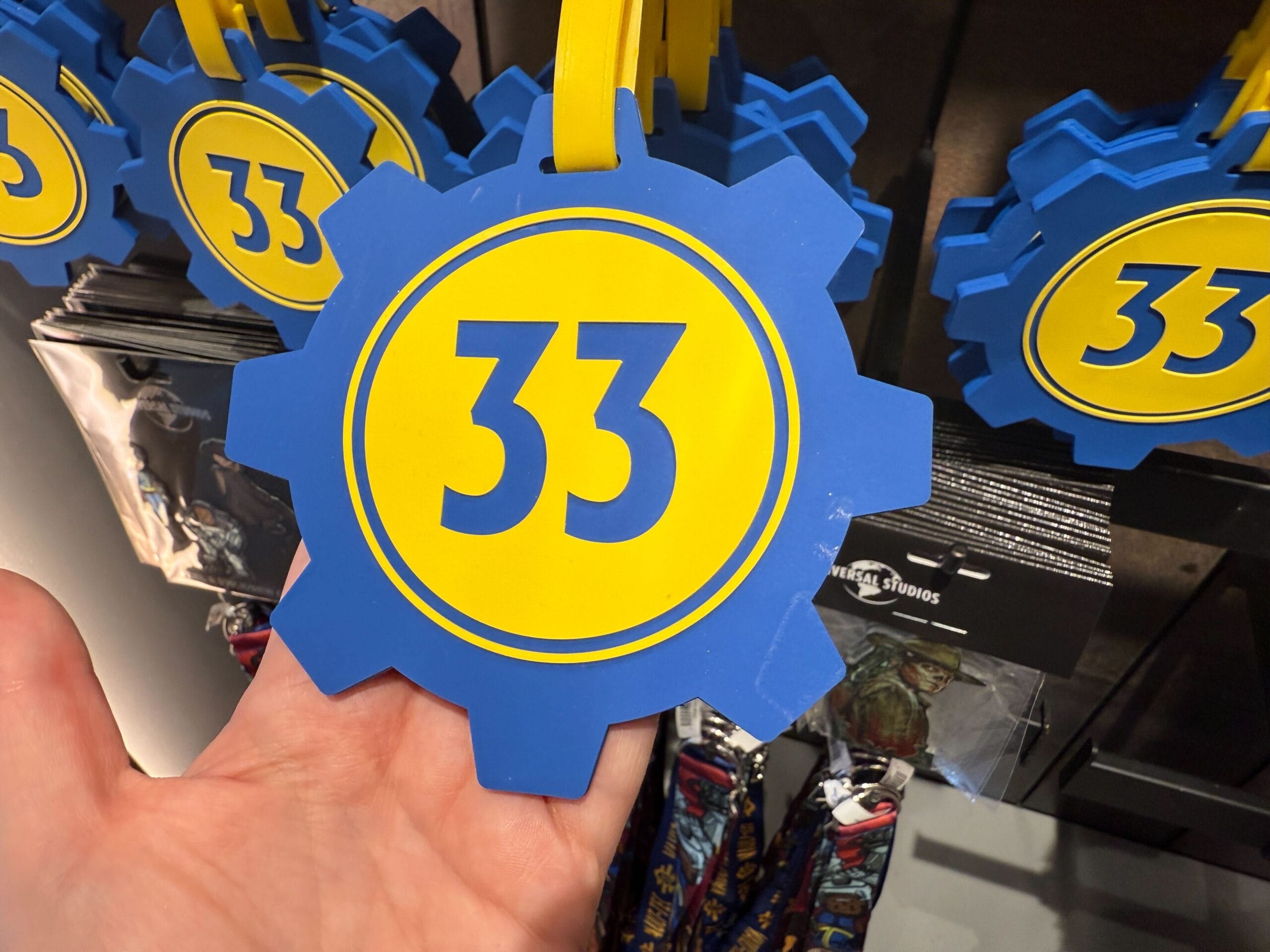 A hand holds a blue gear-shaped tag with a yellow circle and the number 33 in blue at the center.
