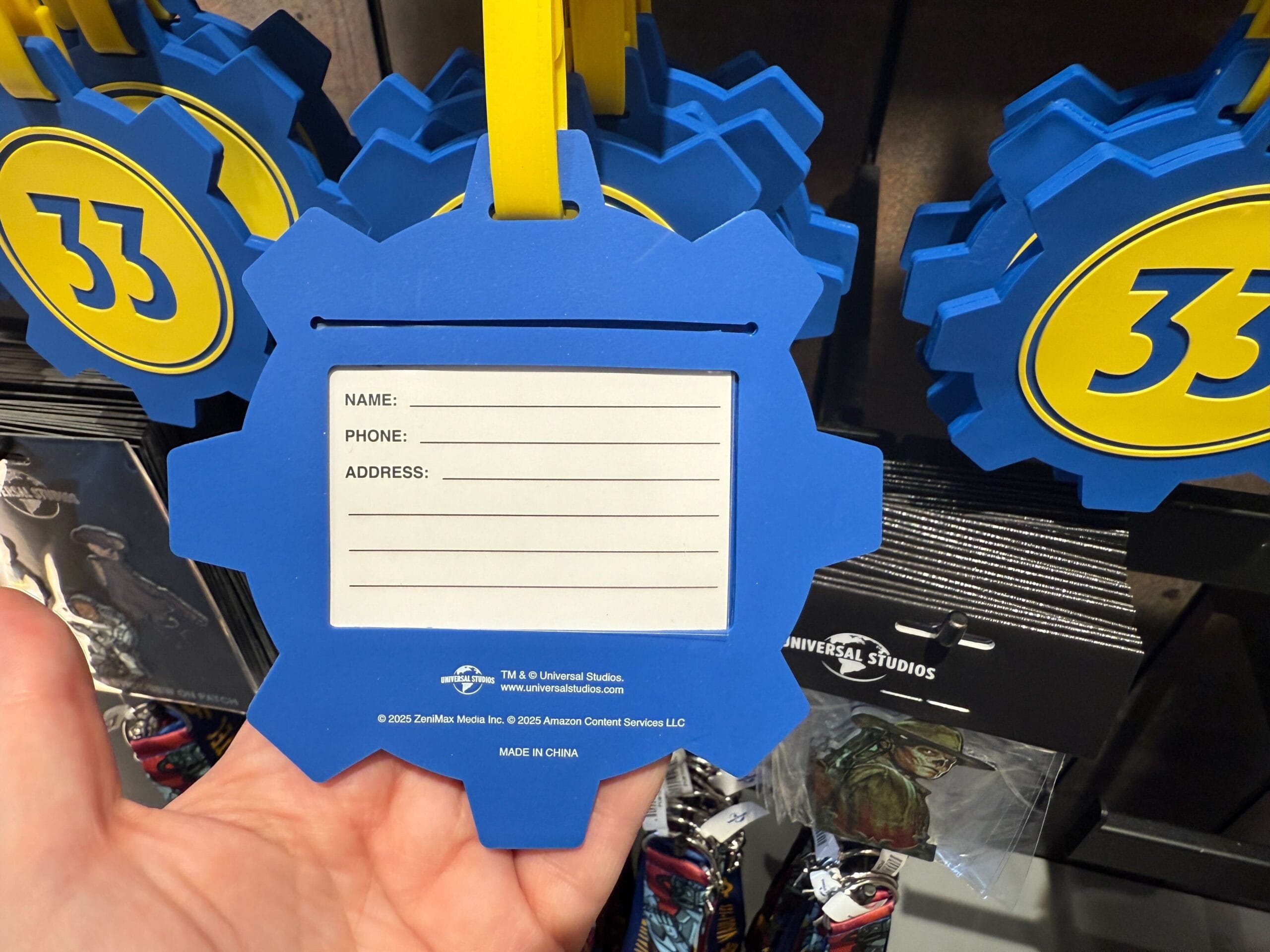 A hand holds a blue gear-shaped luggage tag with spaces for name, phone, and address, labeled "33" on the front.