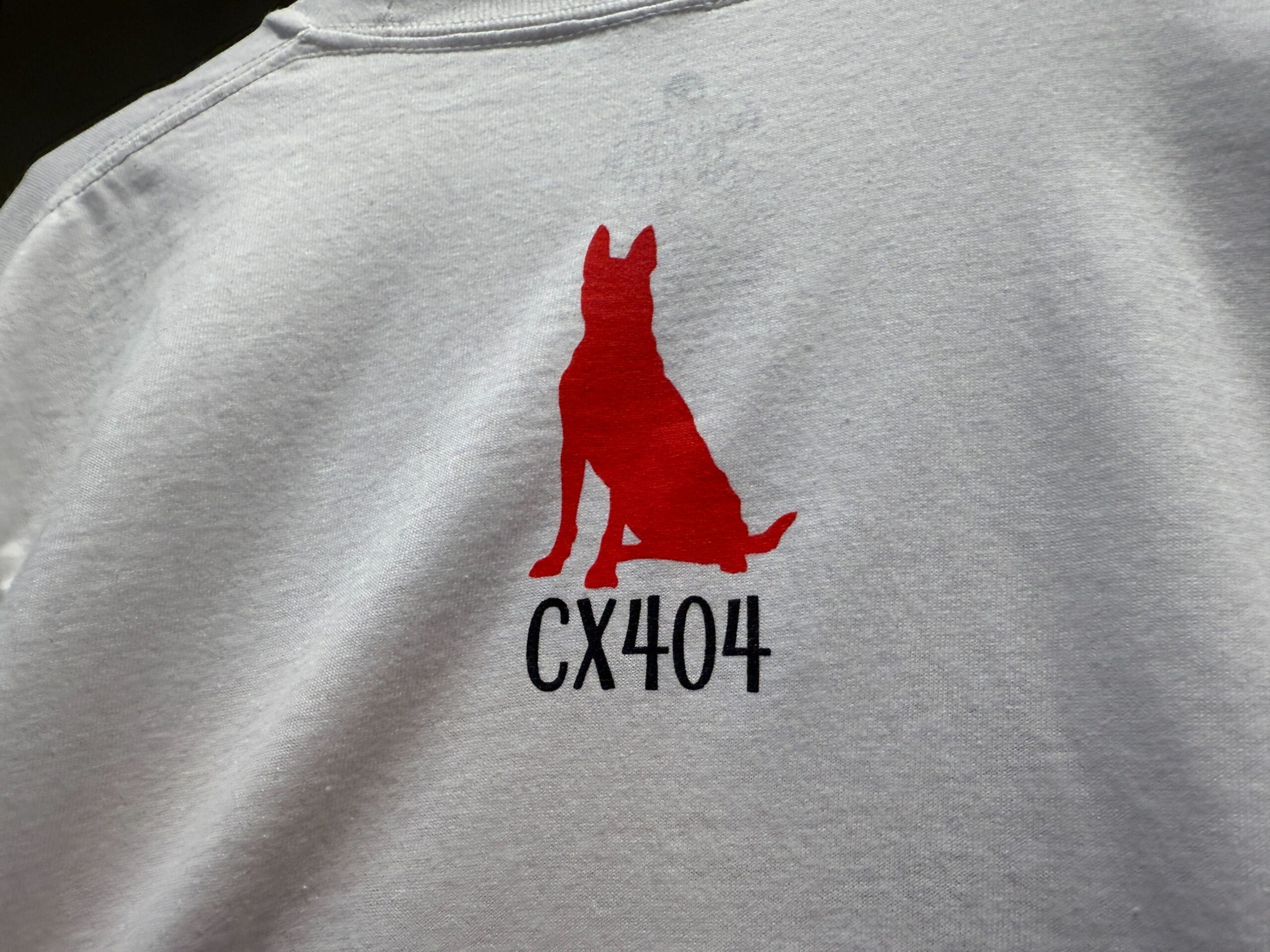 A red silhouette of a sitting dog above the text "CX404" on a light grey shirt.