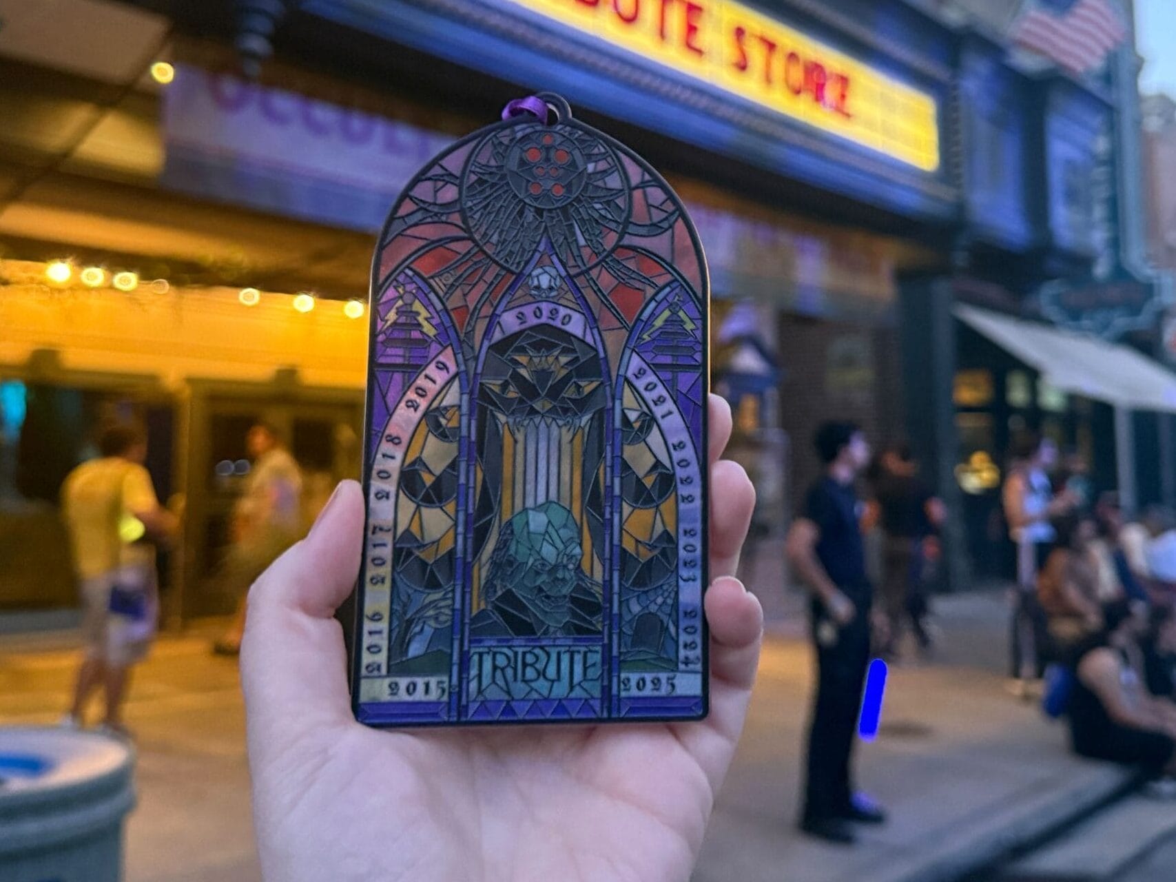 A hand holds a Tribute Store Ornament in stained glass style for the 10th Anniversary of Halloween Horror Nights.