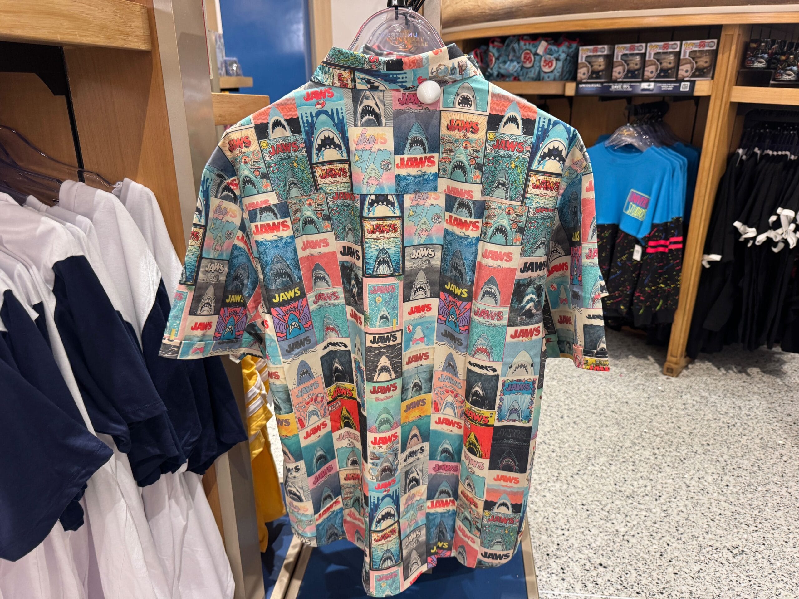 A colorful shirt covered in vintage-style Jaws movie poster prints hangs on a store rack.