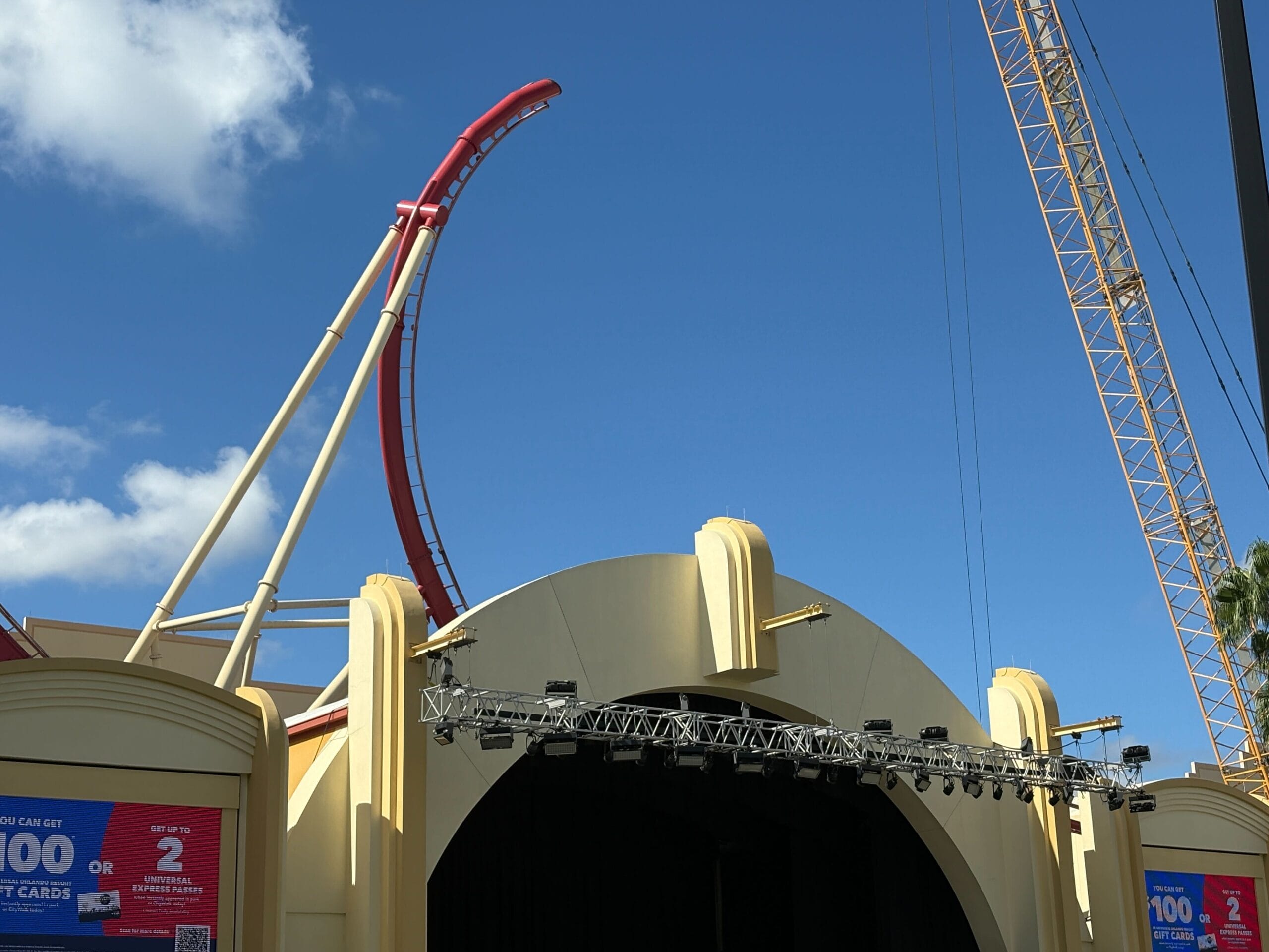 A red Rip Ride Rockit track curves above a yellow building at Universal Studios, set against a clear blue sky.