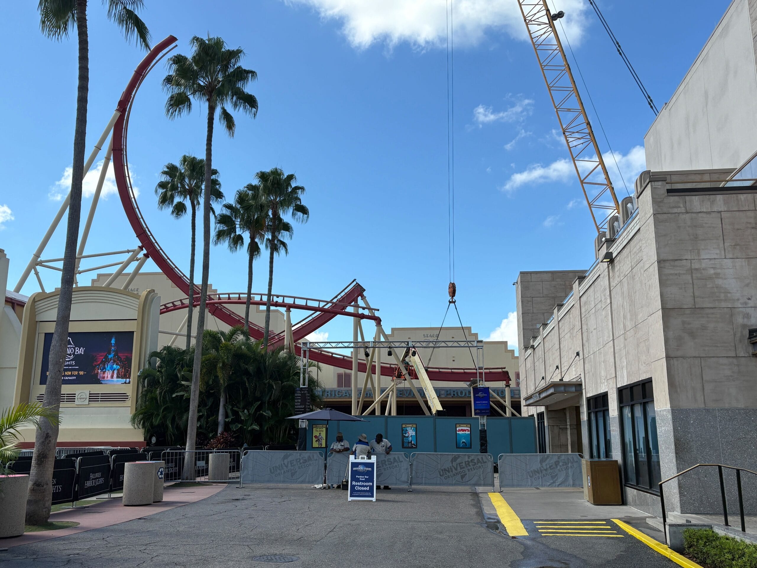 Construction area at Universal Studios with a crane, palm trees, and Rip Ride Rockit tracks under a blue sky.