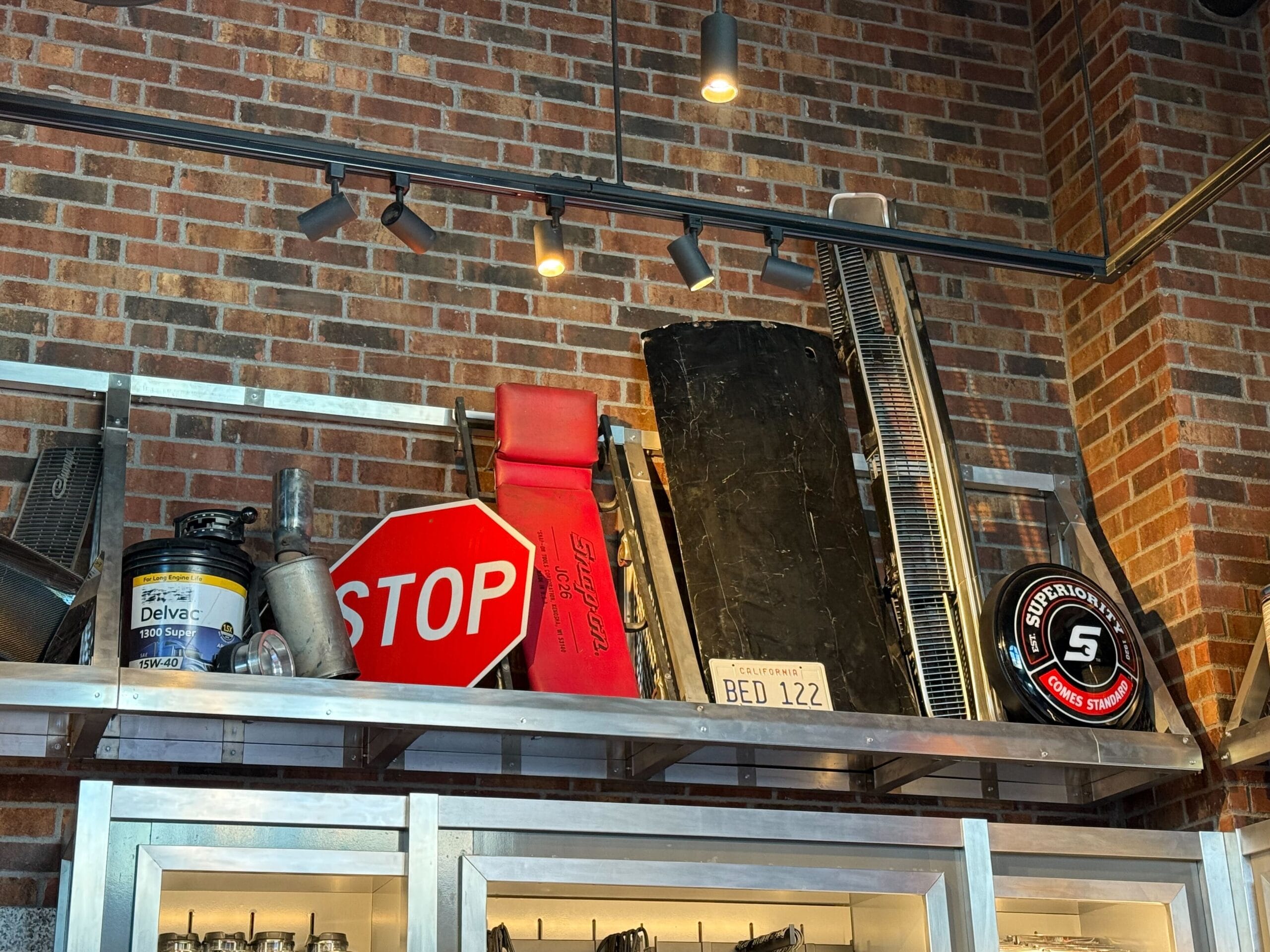 A shelf at the Fast & Furious Store displays car parts, a stop sign, and Fast & Furious merchandise against a brick wall.