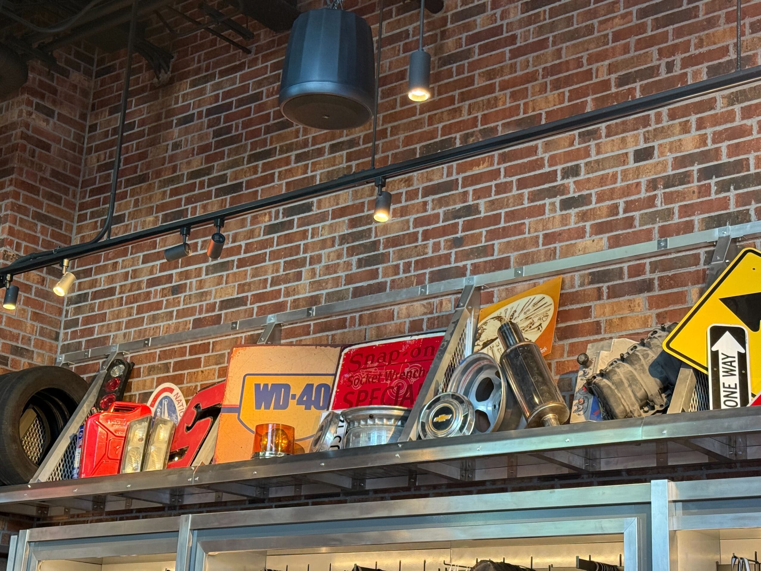 A shelf displays Fast & Furious Store merchandise, a WD-40 box, and tools against a brick wall under track lighting.