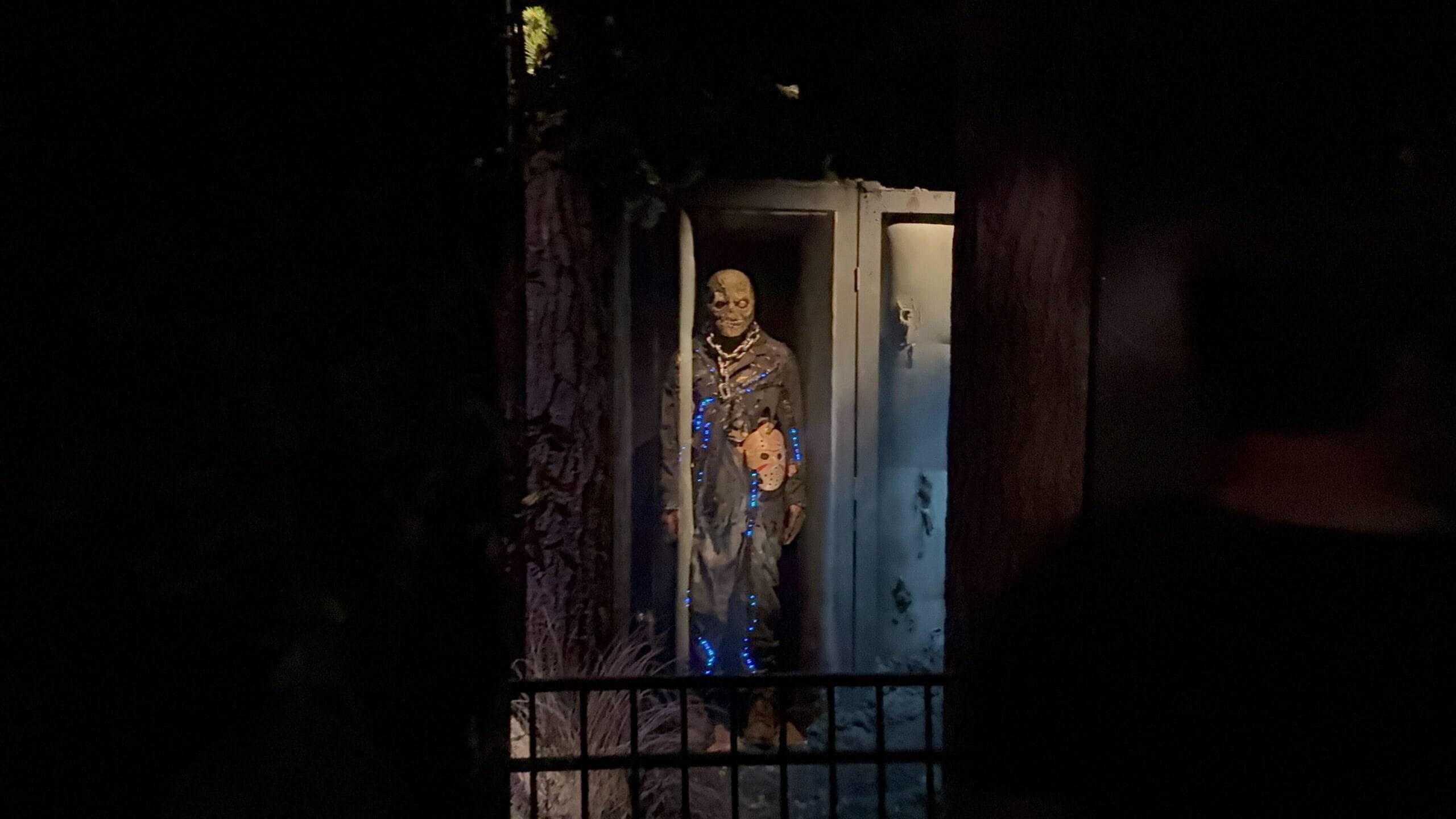 A creepy, zombie-like figure in tattered clothes stands in a dimly lit, eerie outdoor setting at night.