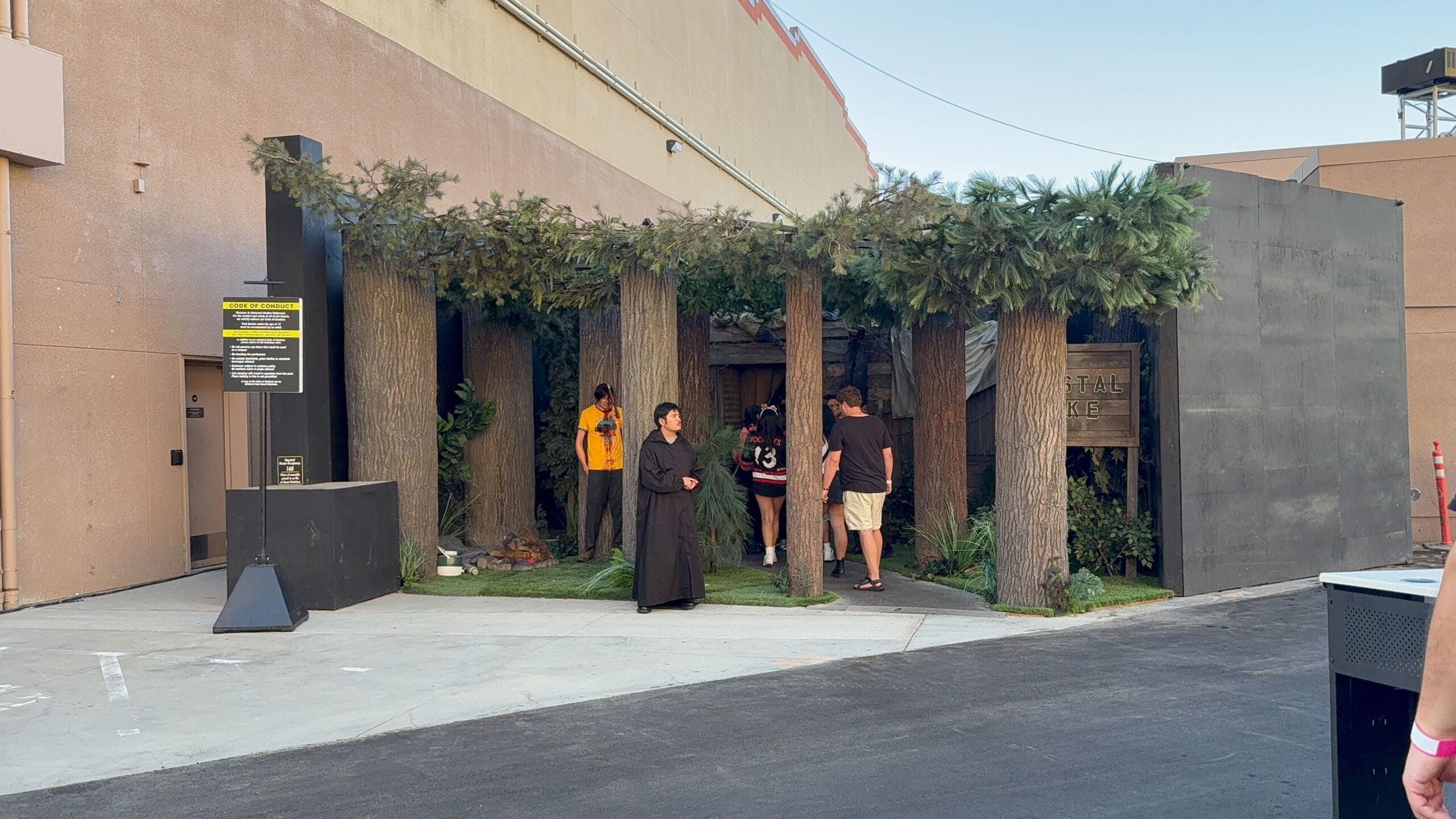 People enter a forest-themed structure outside; a person in a dark robe stands near the entrance.