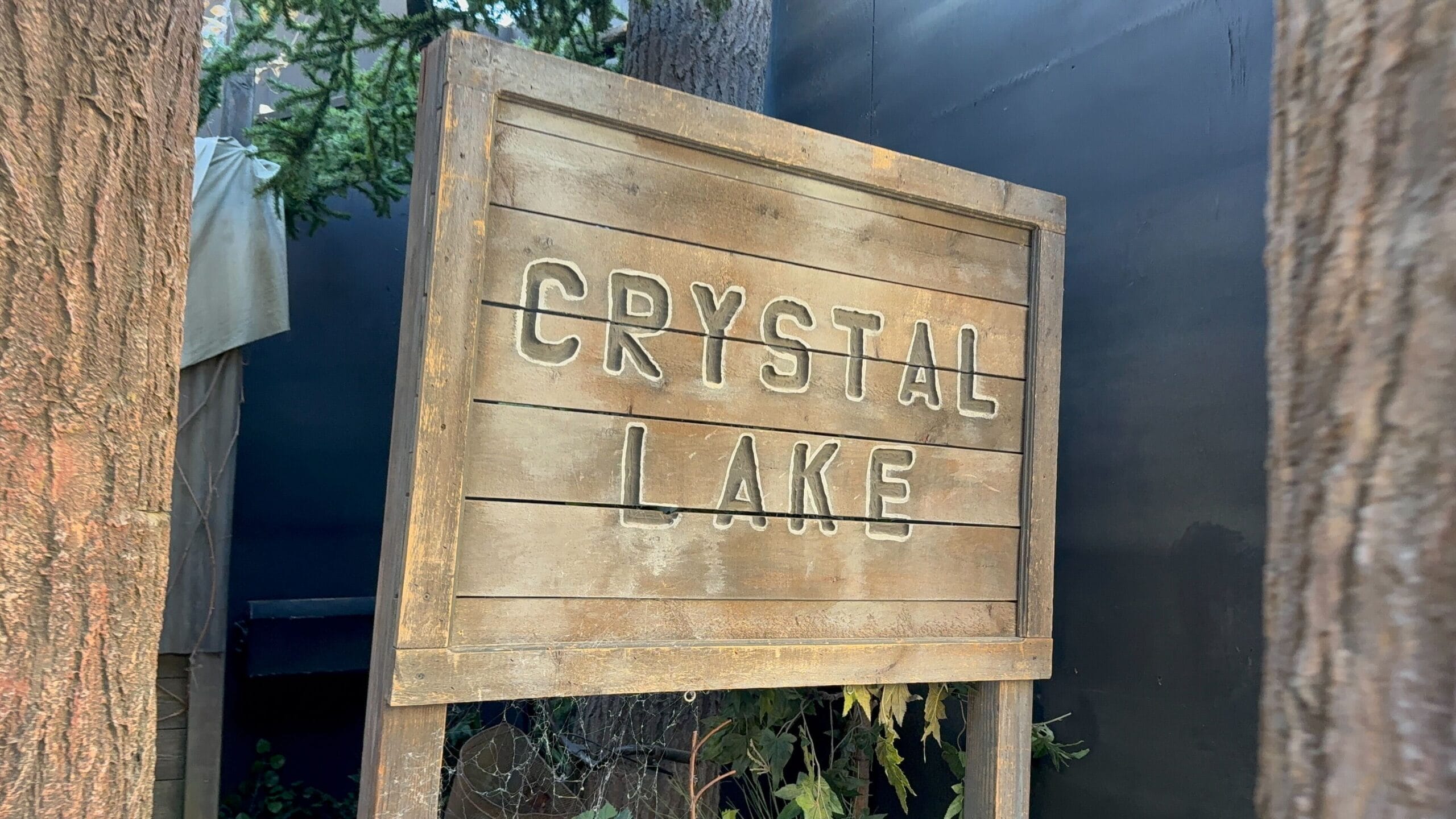 A wooden sign reads "CRYSTAL LAKE" surrounded by trees and greenery.
