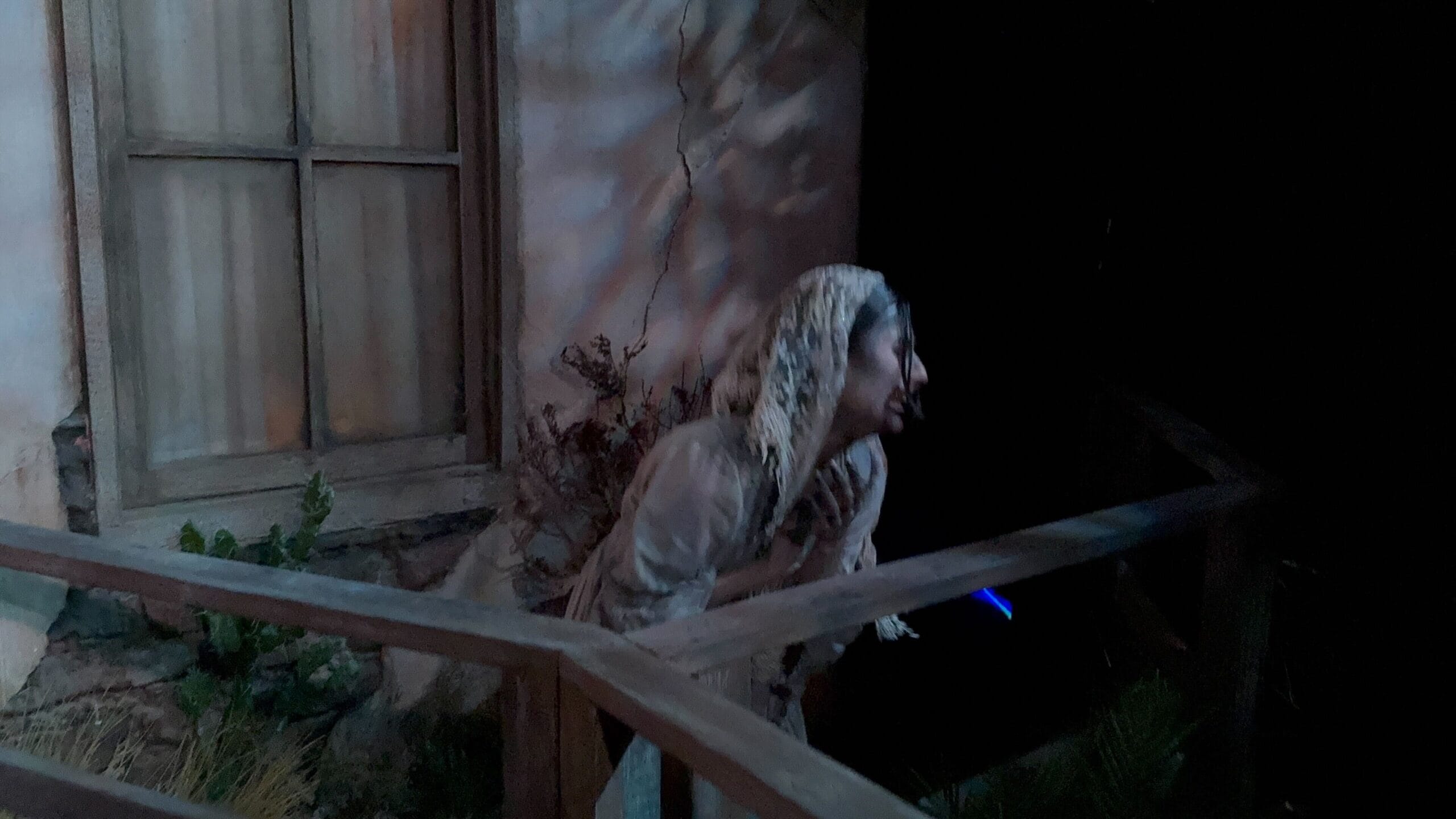A person in old-fashioned clothes and a headscarf leans over a wooden railing at night at USH’s Monstros 3 for HHN 2025.