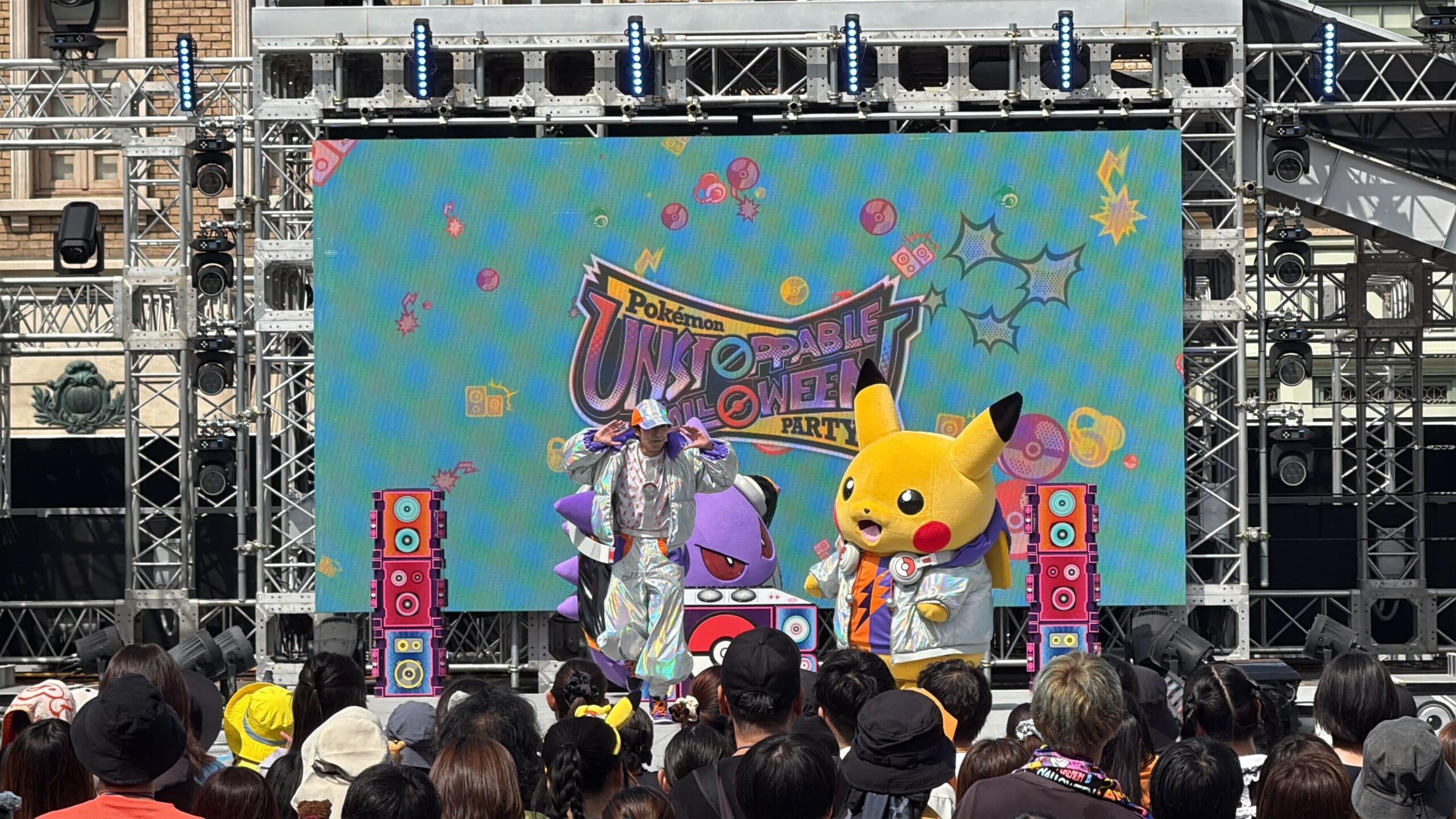 A crowd enjoys performers and a Pikachu mascot onstage at a colorful Pokémon Halloween Party at Universal Studios Japan.