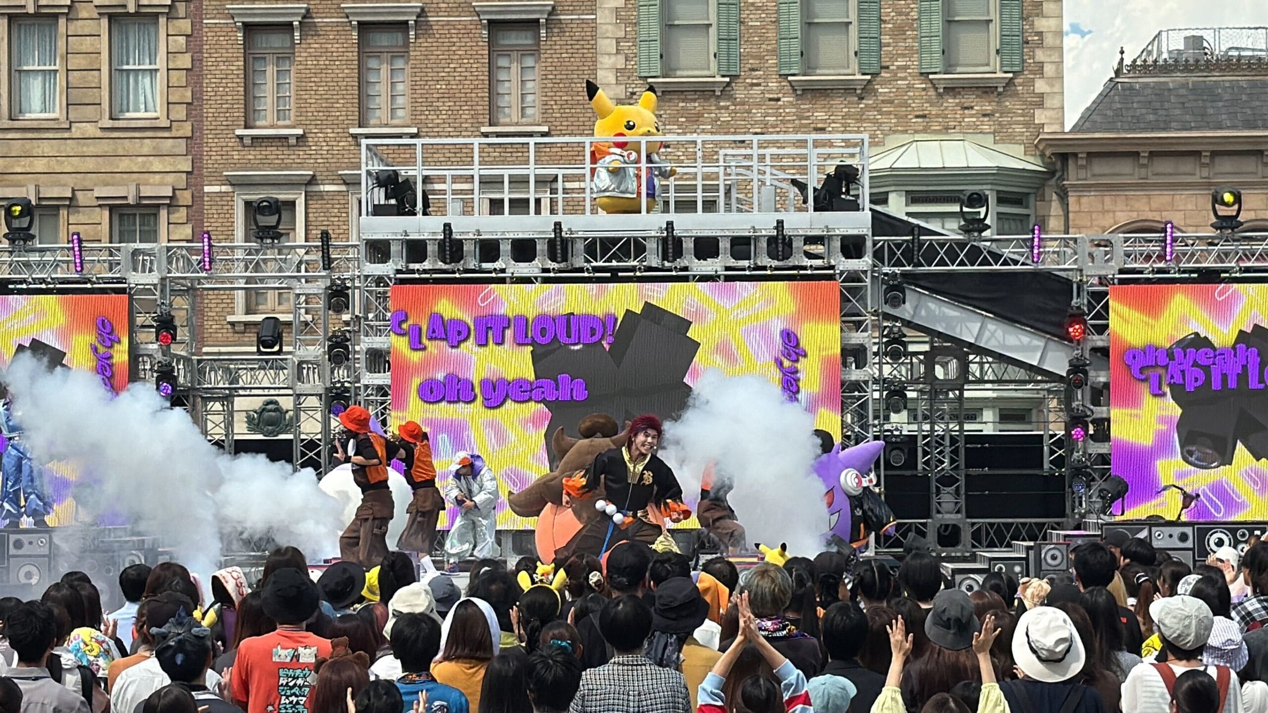 Stage performance at Universal Studios Japan: Pikachu mascot above dancers, “Lap ft LOUD! Oh yeah” screens, Halloween Party crowd below.
