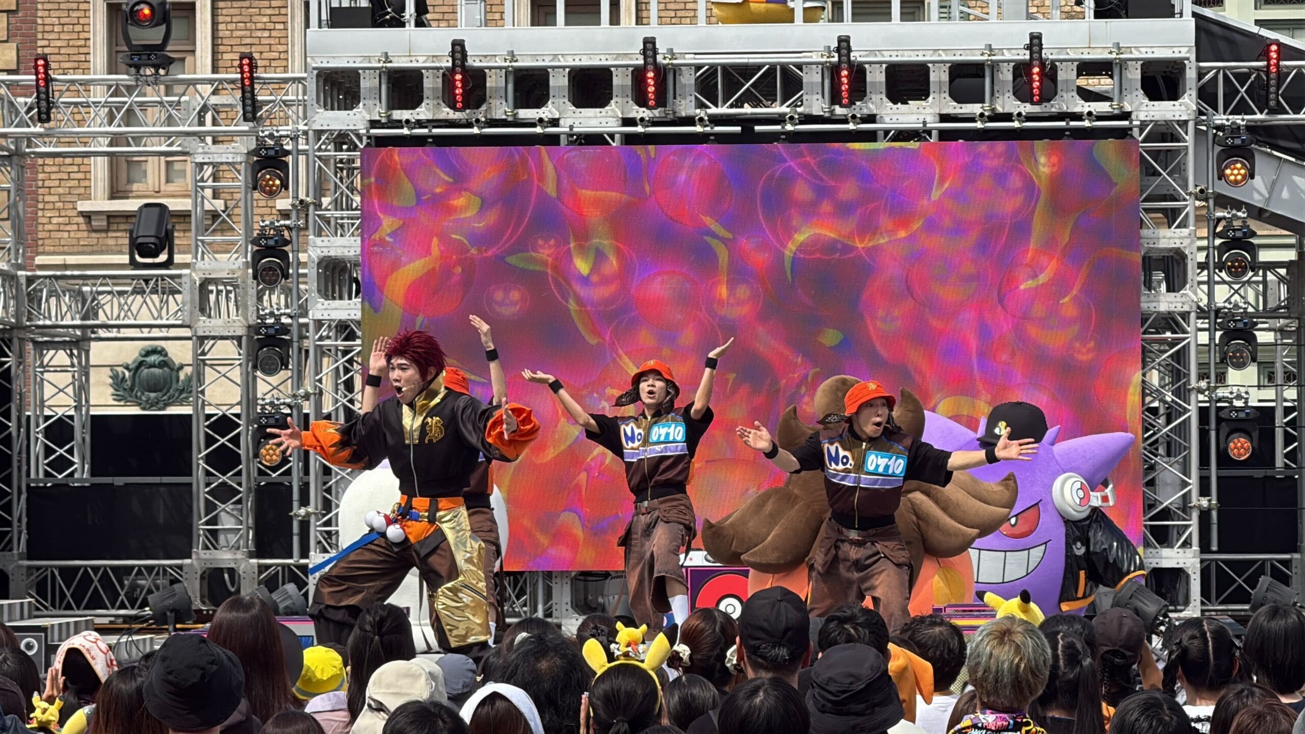 Three dancers perform energetically onstage at the Pokémon Halloween Party, dazzling a large Universal Studios Japan crowd.