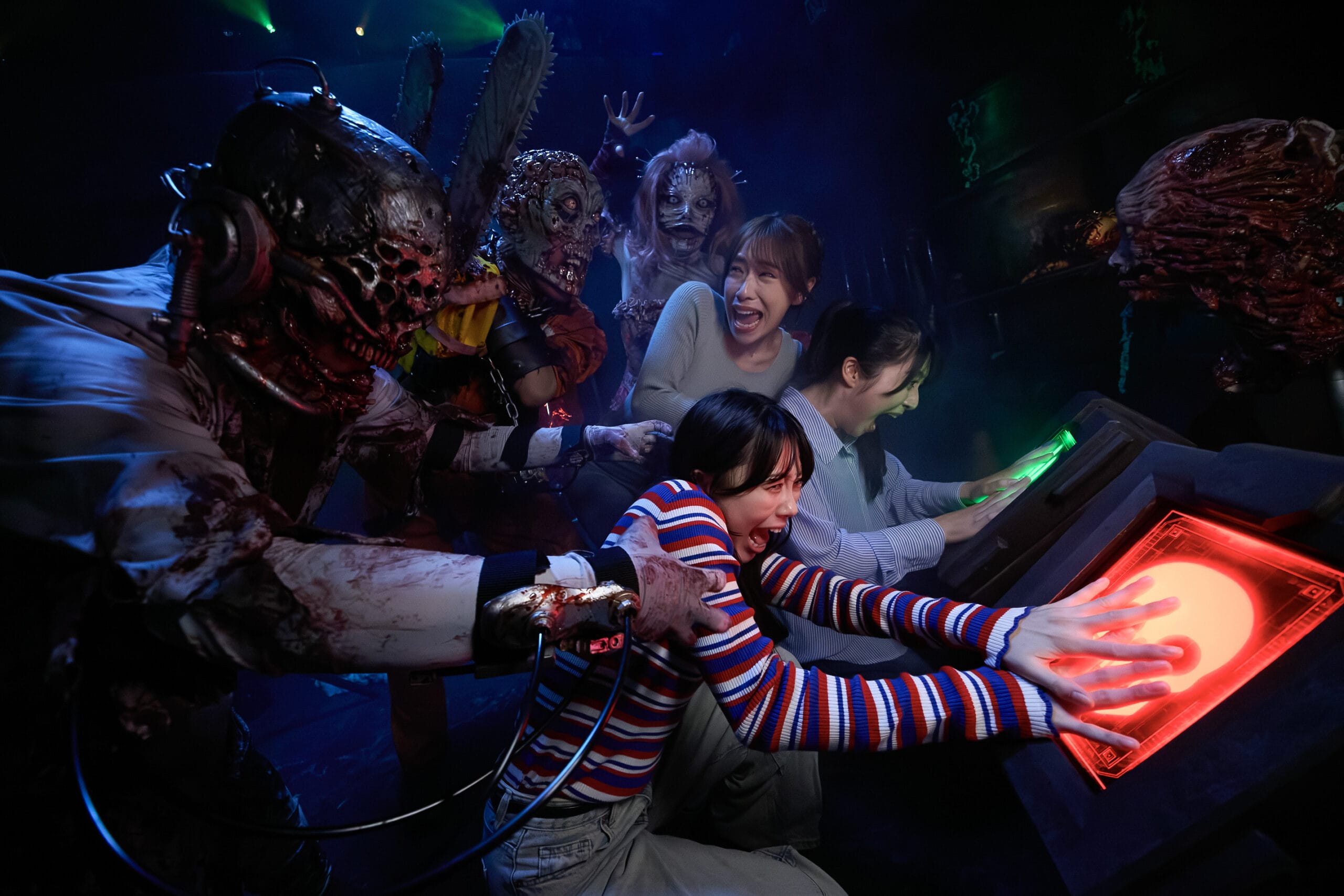 Two terrified women press glowing buttons as gruesome monsters stalk them in the Haunted House at Universal Studios Japan.