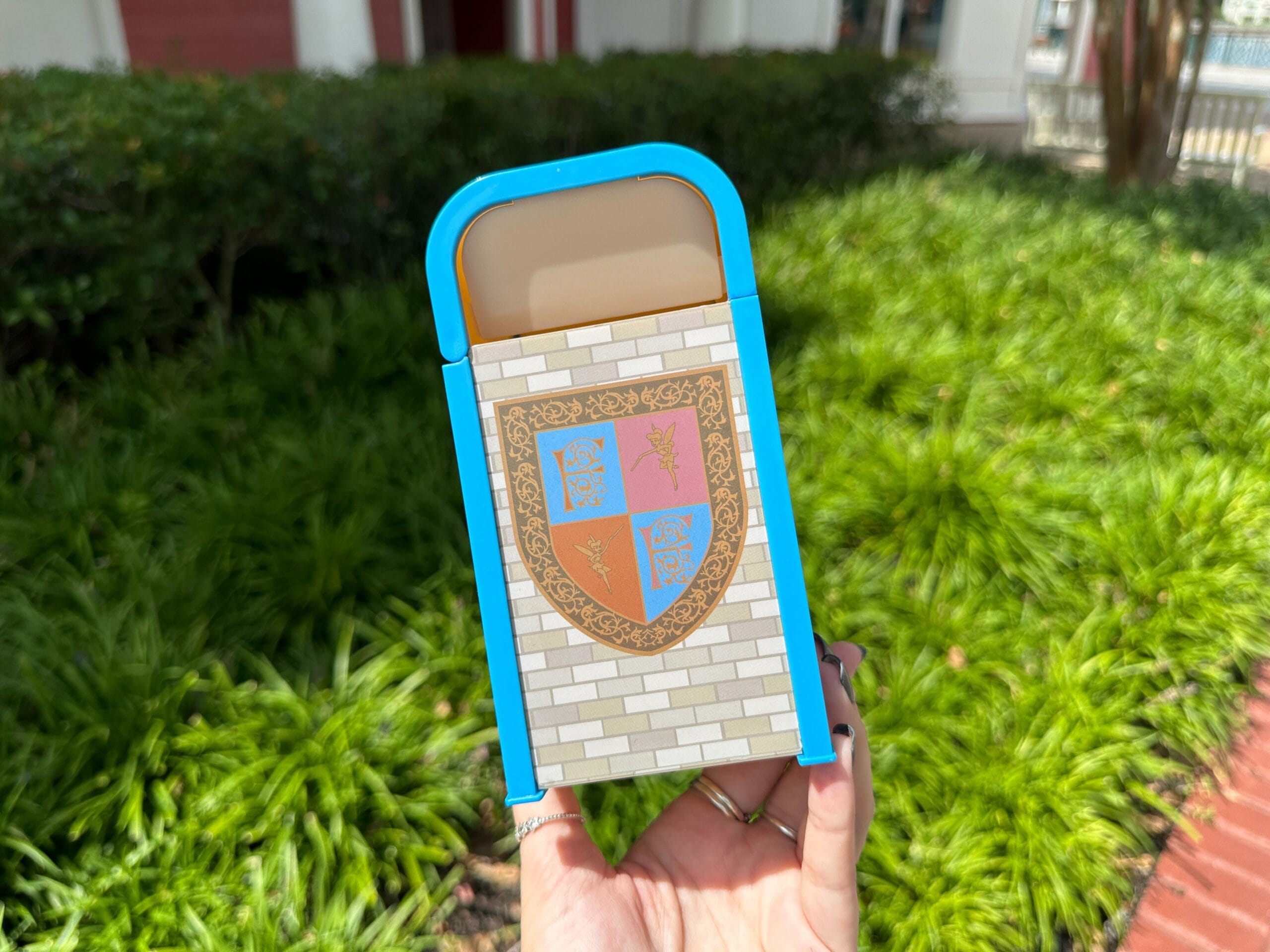 A hand holds a decorative box with blue accents and a gold crest, inspired by the Fantasyland Trash Can at Disney World.