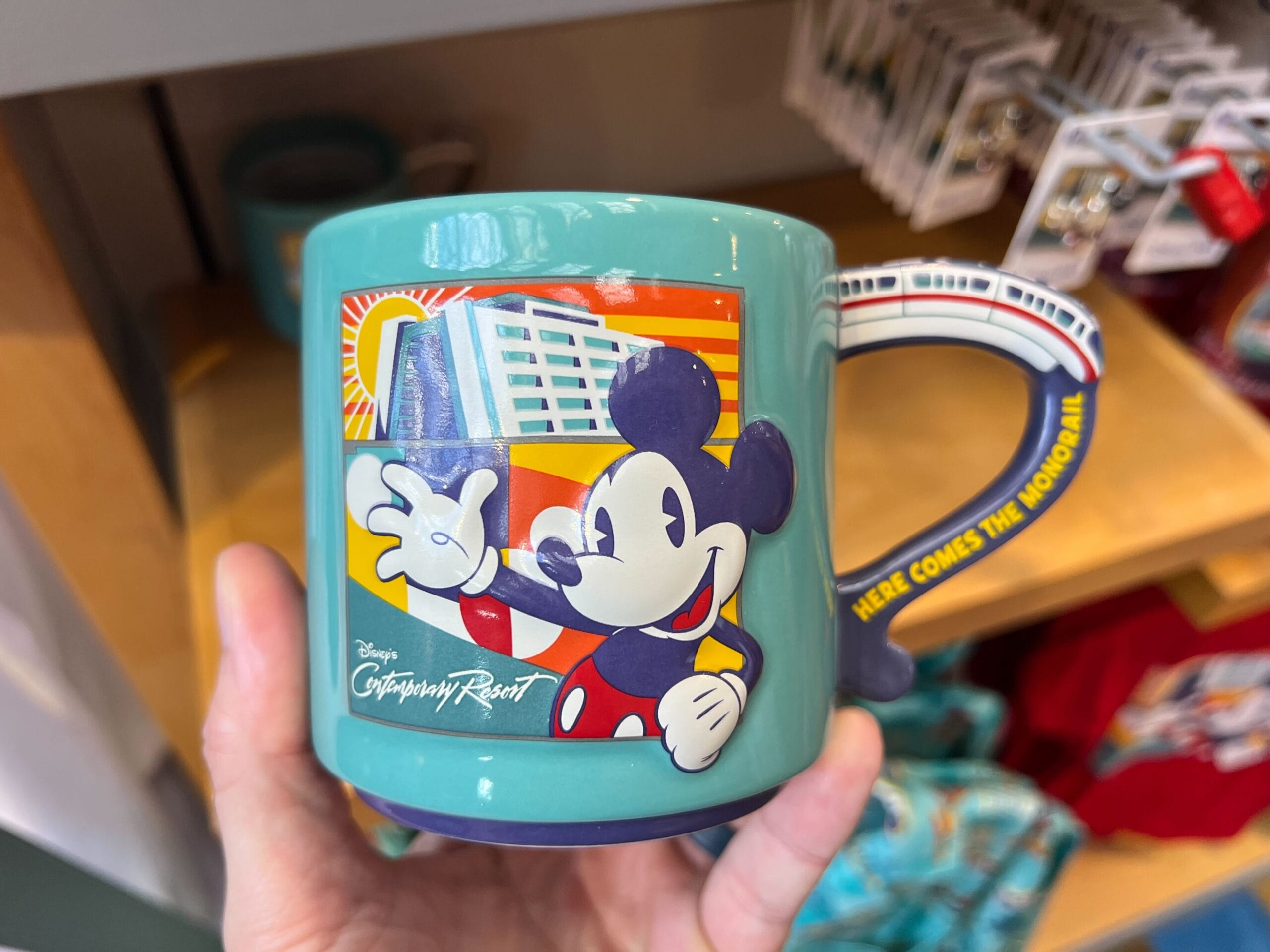 A teal mug from the Monorail Collection featuring Mickey Mouse and Disney’s Contemporary Resort, monorail handle included.