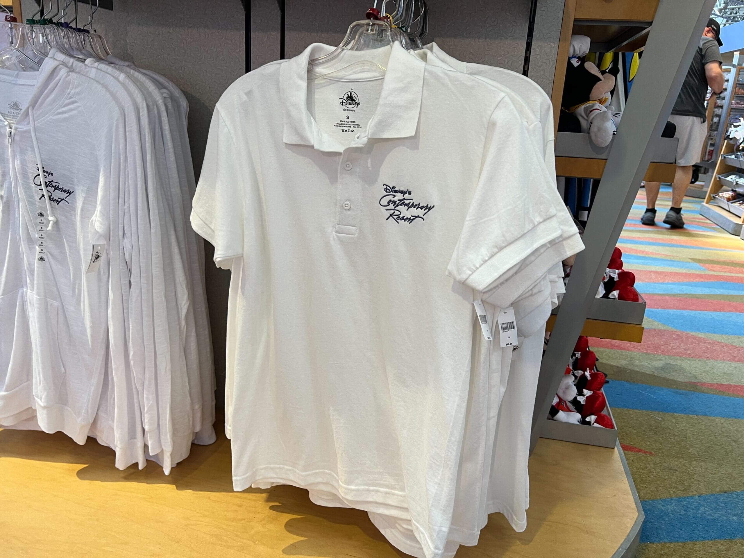 White polo shirts on display, part of the Monorail Collection, embroidered with "Disney's Contemporary Resort" in blue.