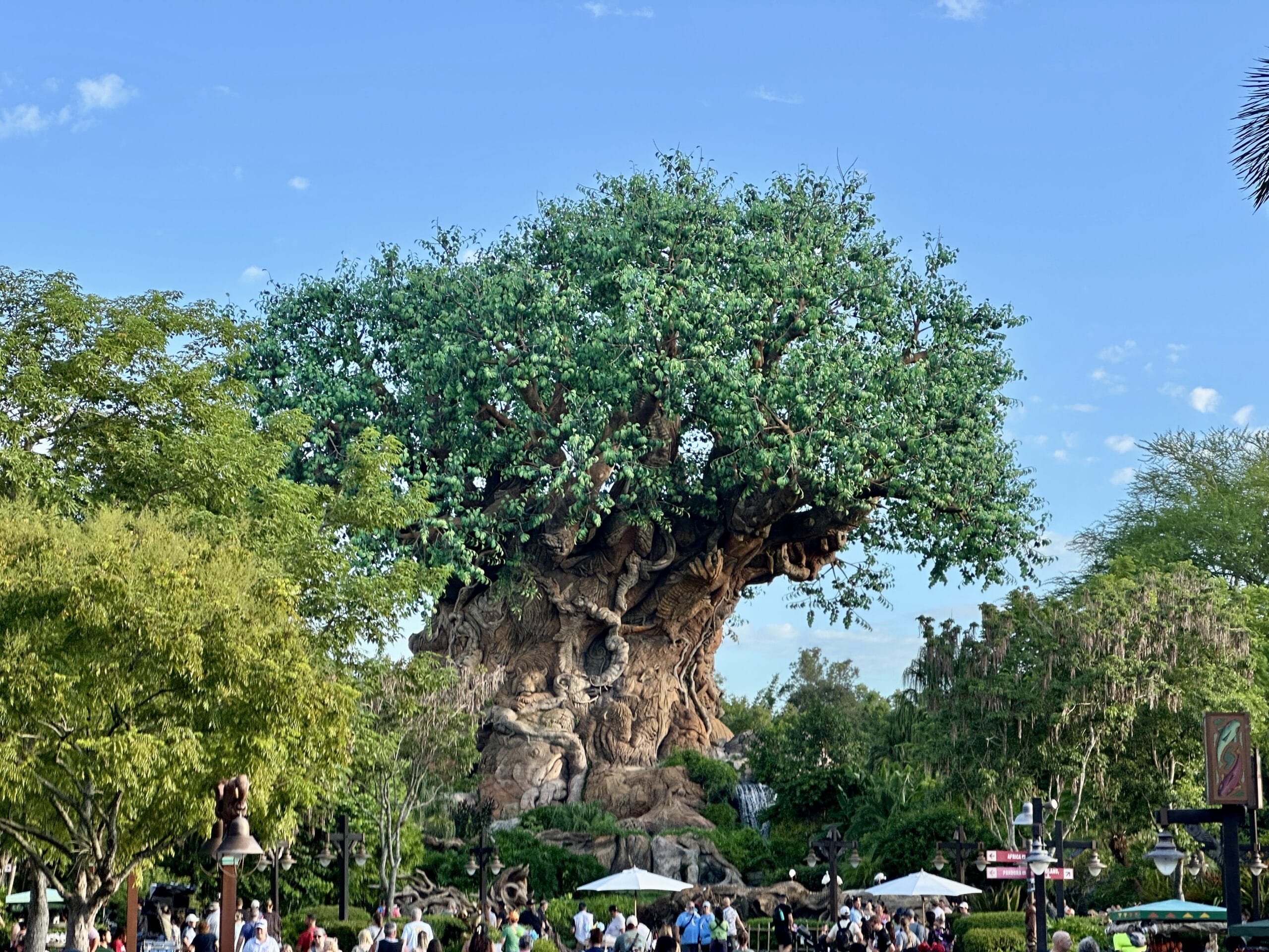 Large artificial tree with carved animal figures at Disney's Animal Kingdom, surrounded by lush greenery and visitors.
