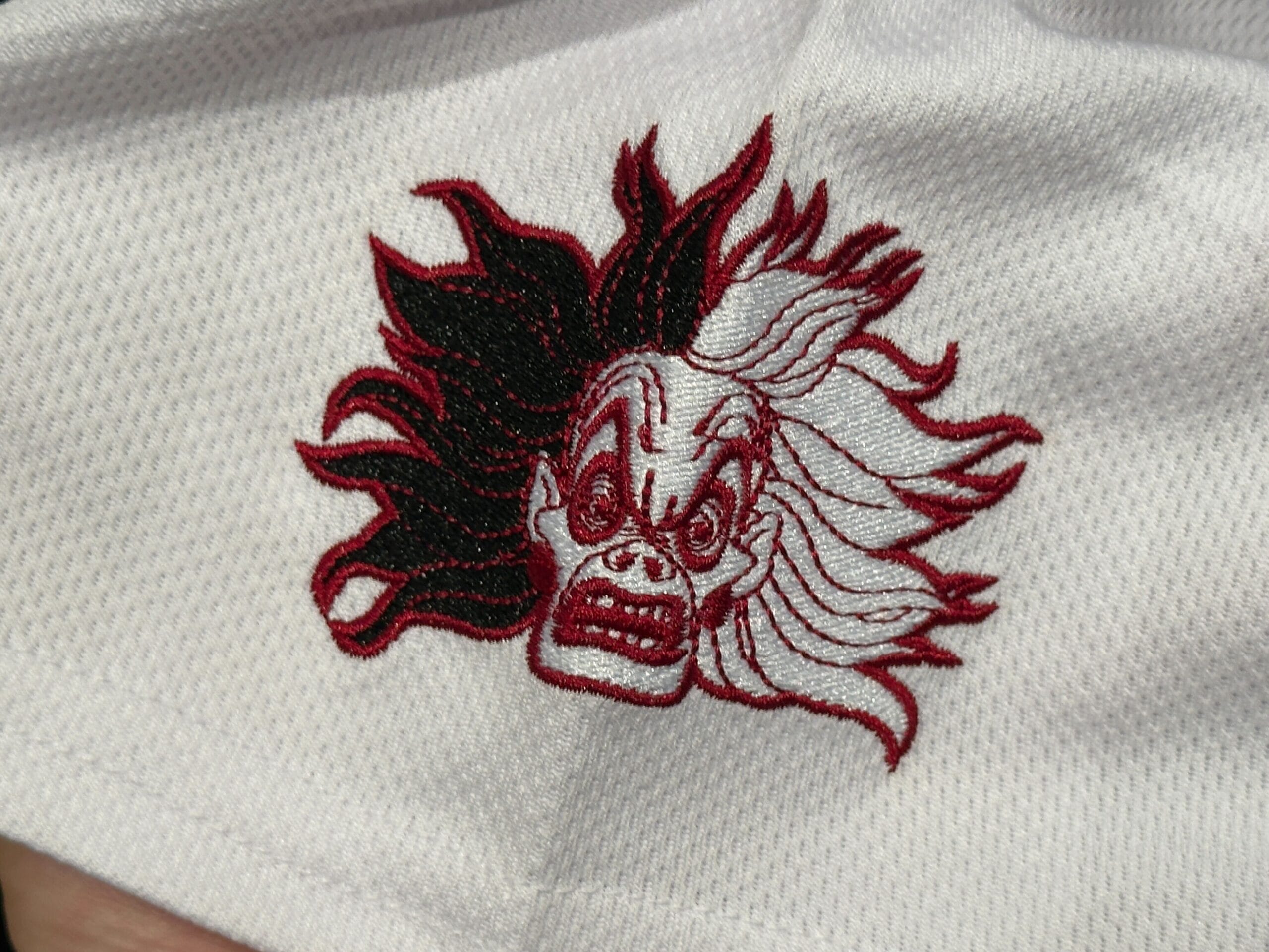 Embroidered patch of a split-tone scary face with wild hair, inspired by Cruella de Vil, on white fabric.