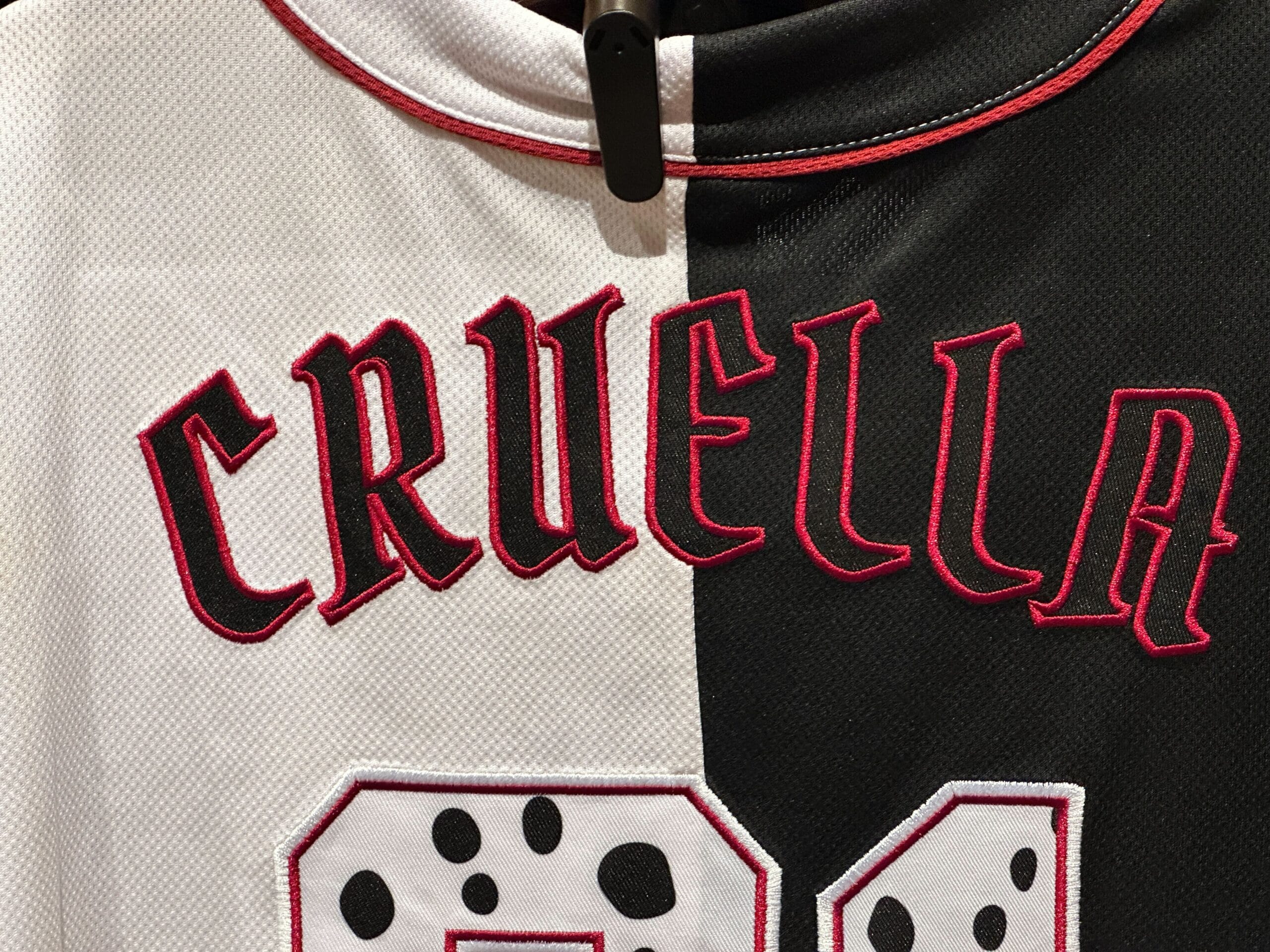 A Cruella de Vil baseball jersey with "CRUELLA" in red, split black and white, and a Dalmatian spot pattern below.