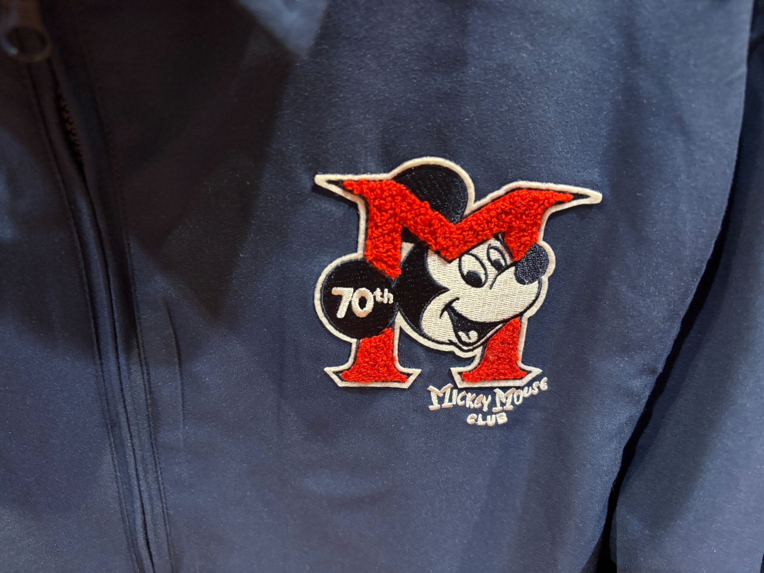 Embroidered Mickey Mouse Club 70th Collection logo on a dark blue jacket.