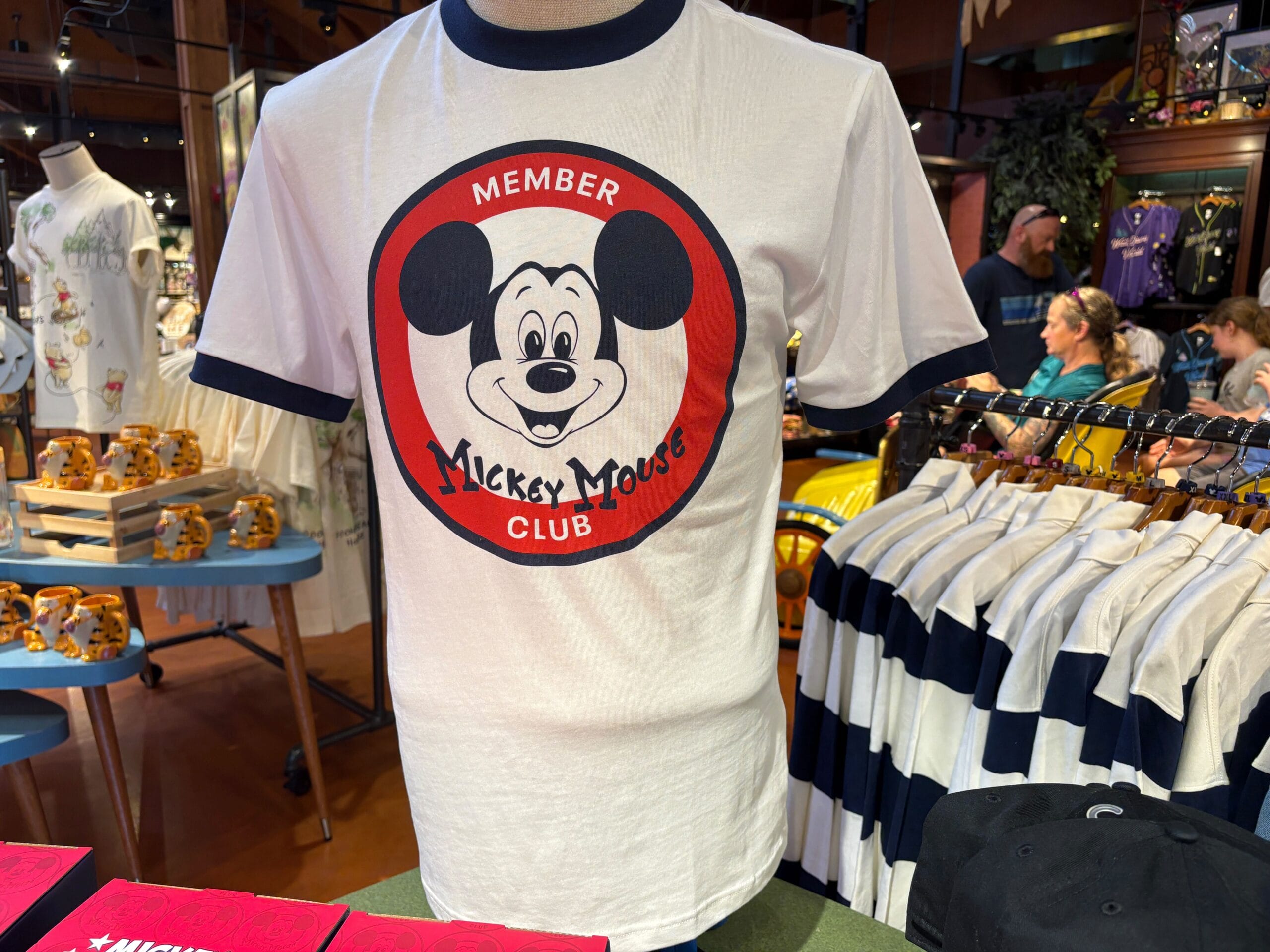 White T-shirt from the Mickey Mouse Club 70th Collection with “Member” text, displayed on a store mannequin.