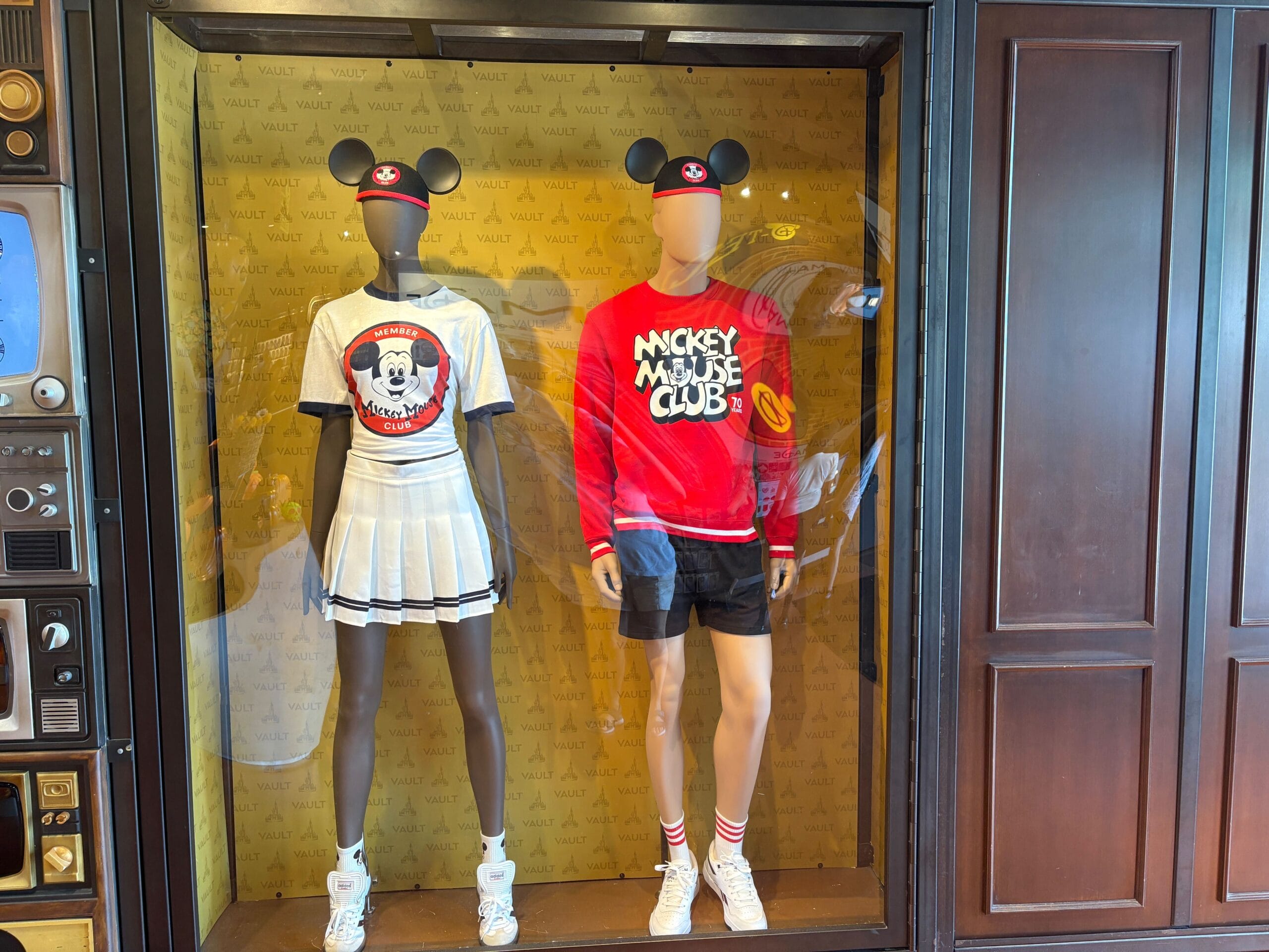 Two mannequins showcase Mickey Mouse Club 70th Collection outfits and ears in a display window.