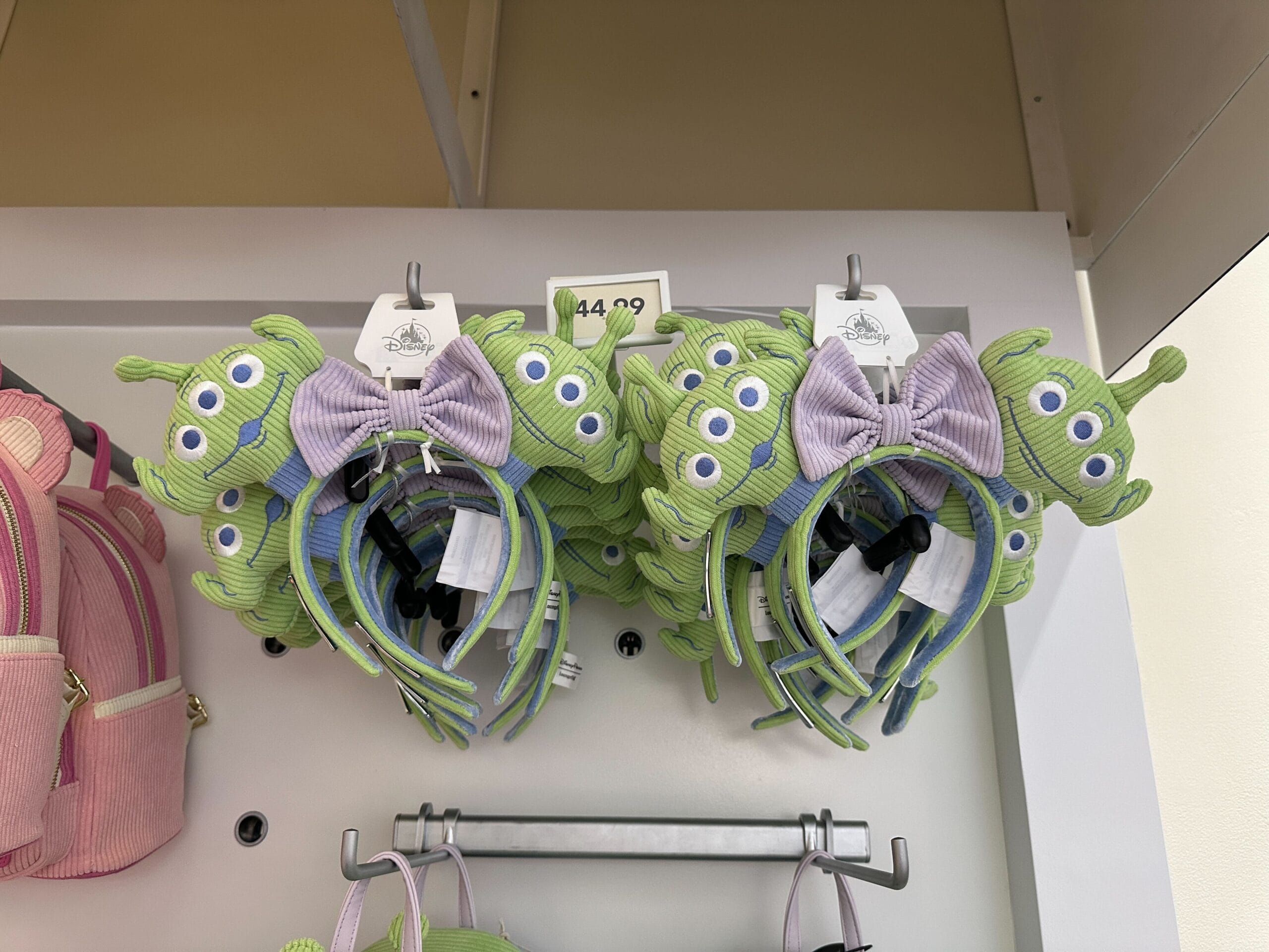 Pastel Toy Story Alien headbands with purple bows are displayed on a store shelf, ready for Disney World fans.