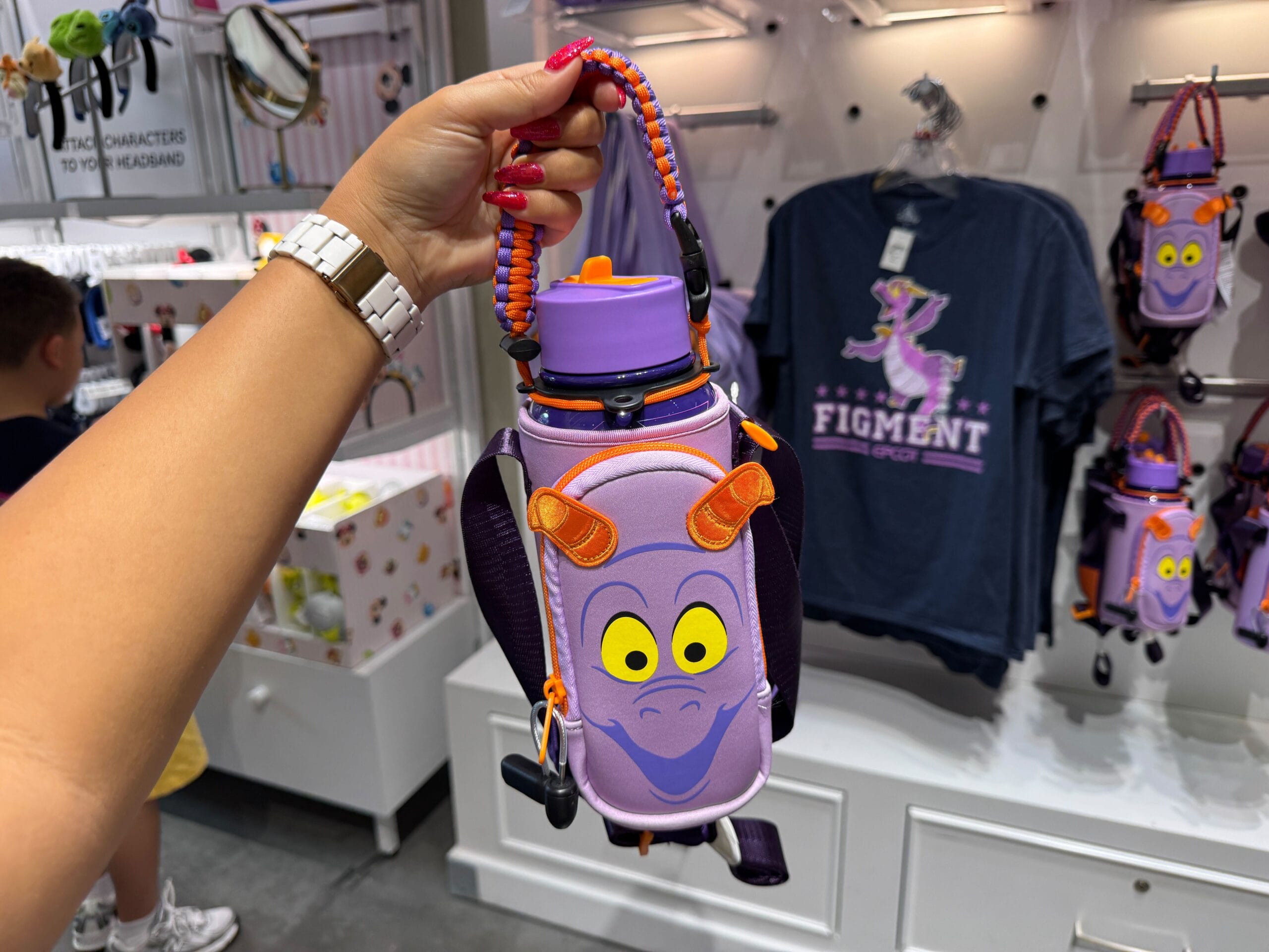 A hand holds a purple Figment water bottle holder in a store filled with imagination and Figment-themed merchandise.