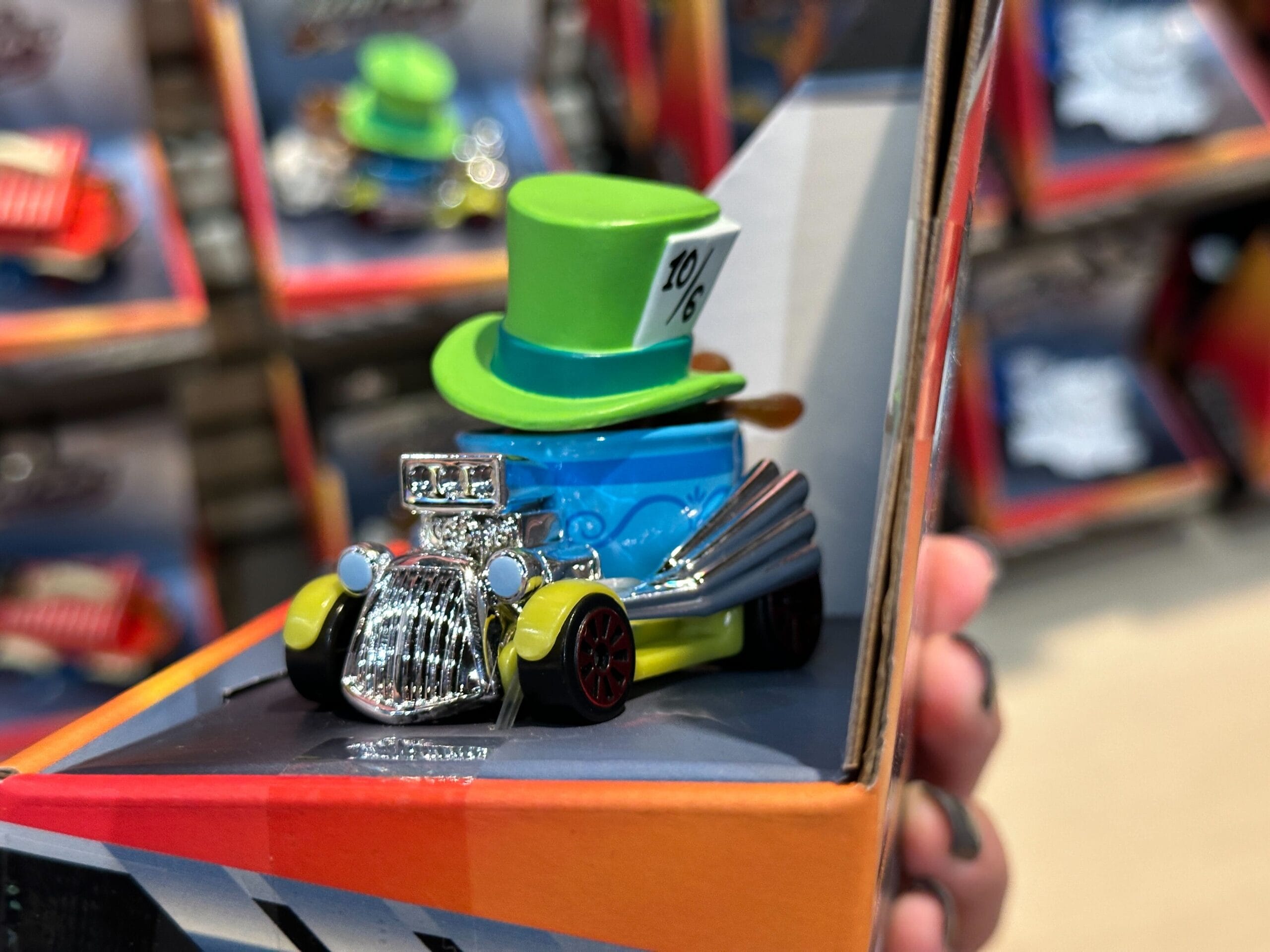 A Disney Racers Toy car with a green "10/6" top hat, held in hand at a Disney World store display.