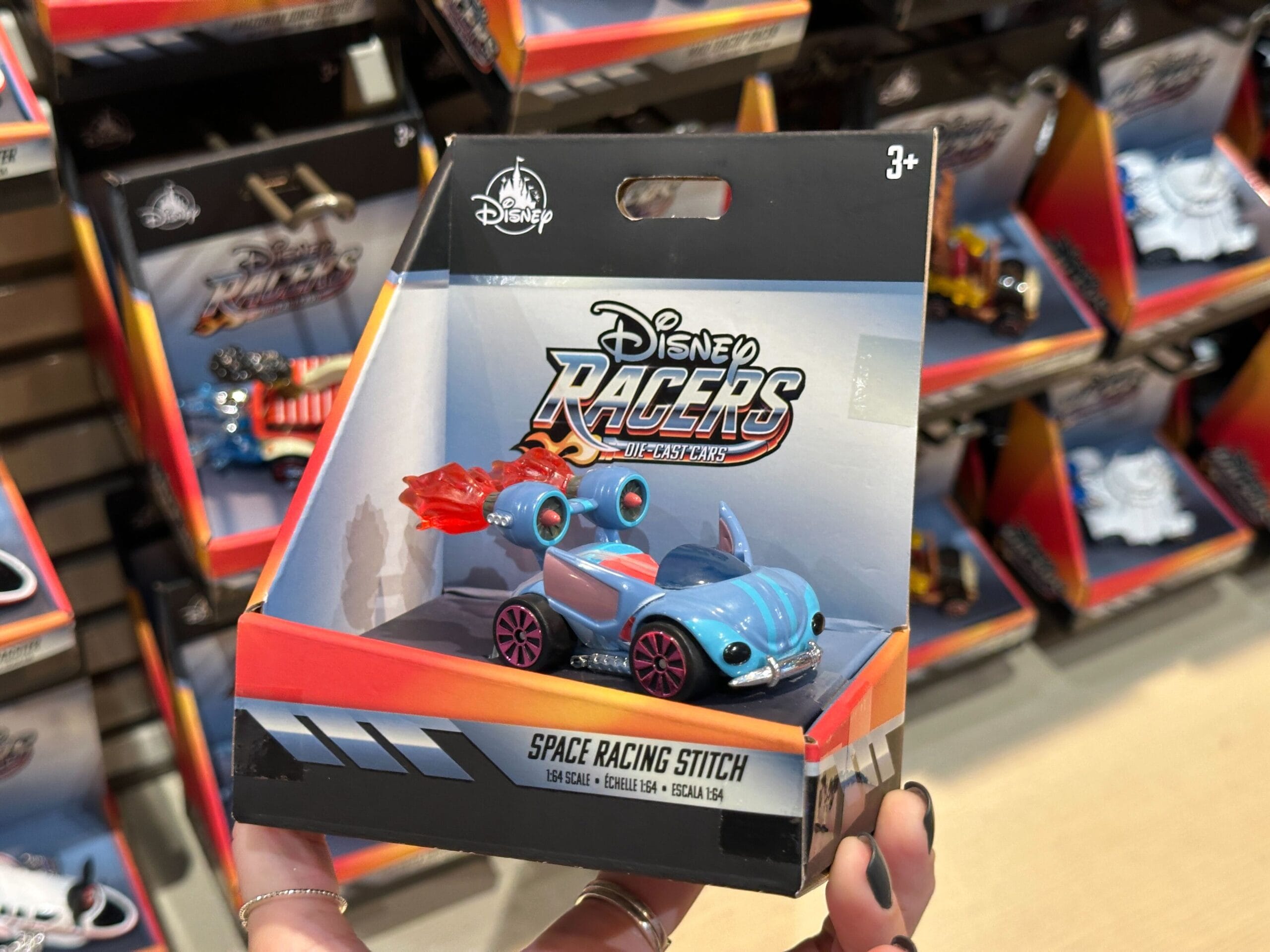 A hand holds a Disney Racers Space Racing Stitch toy car in its packaging at a Disney World store display.