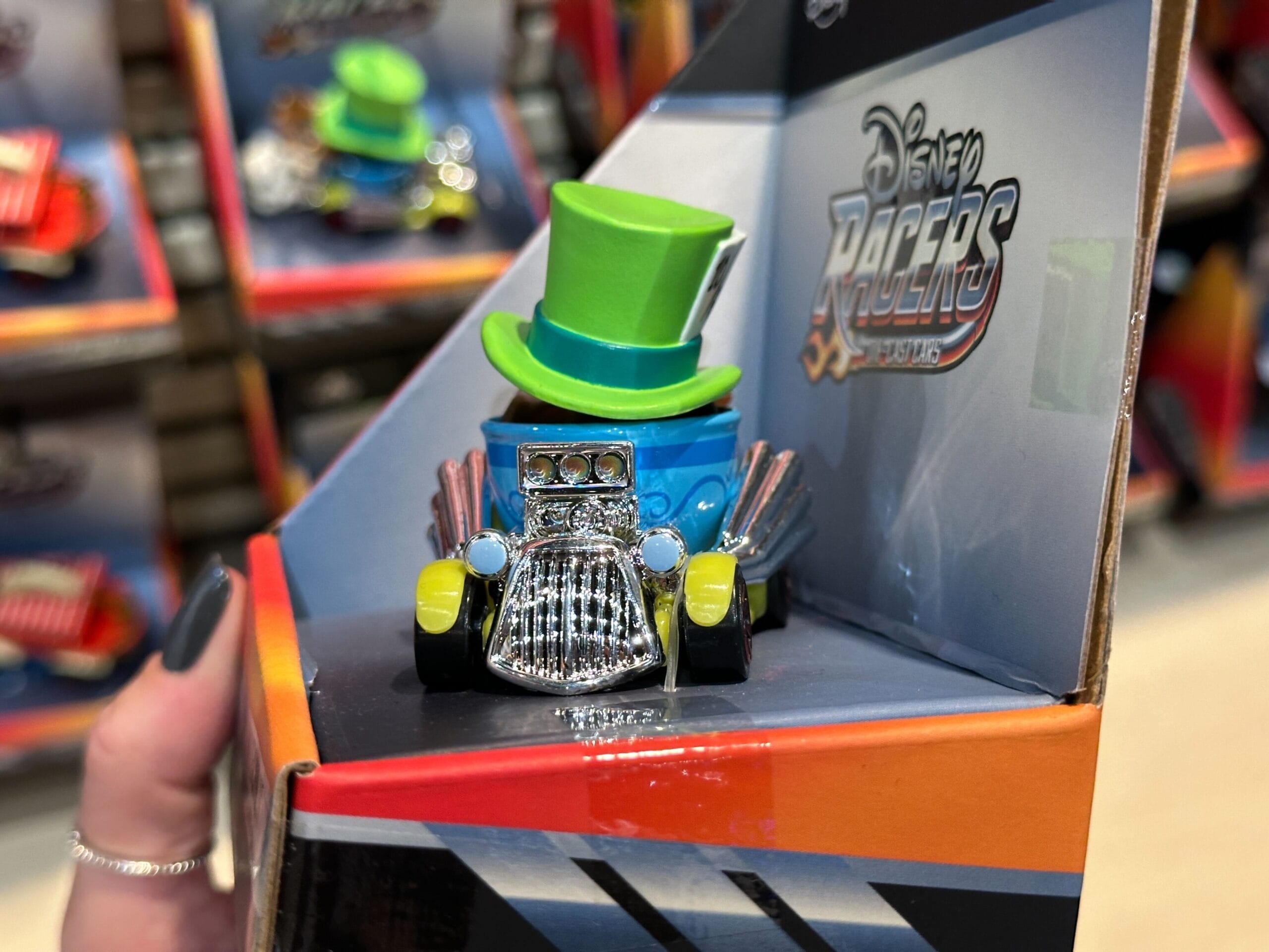 A Disney Racers toy race car with a green top hat, held by gray-polished nails, channels Jungle Cruise flair.