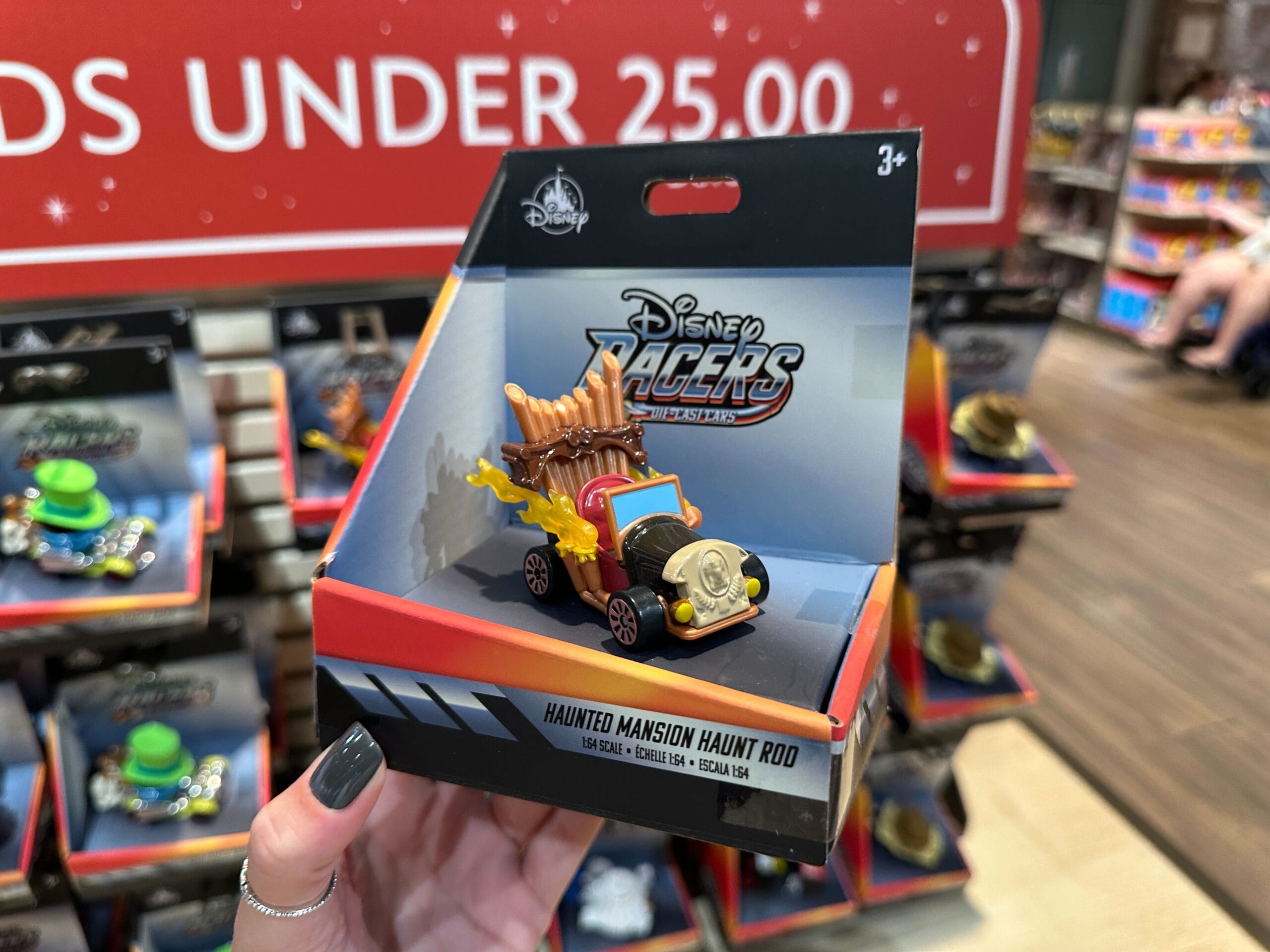 A hand holds a Disney Racers Toy Haunt Rod in a store at Disney World, with hats on shelves in the background.