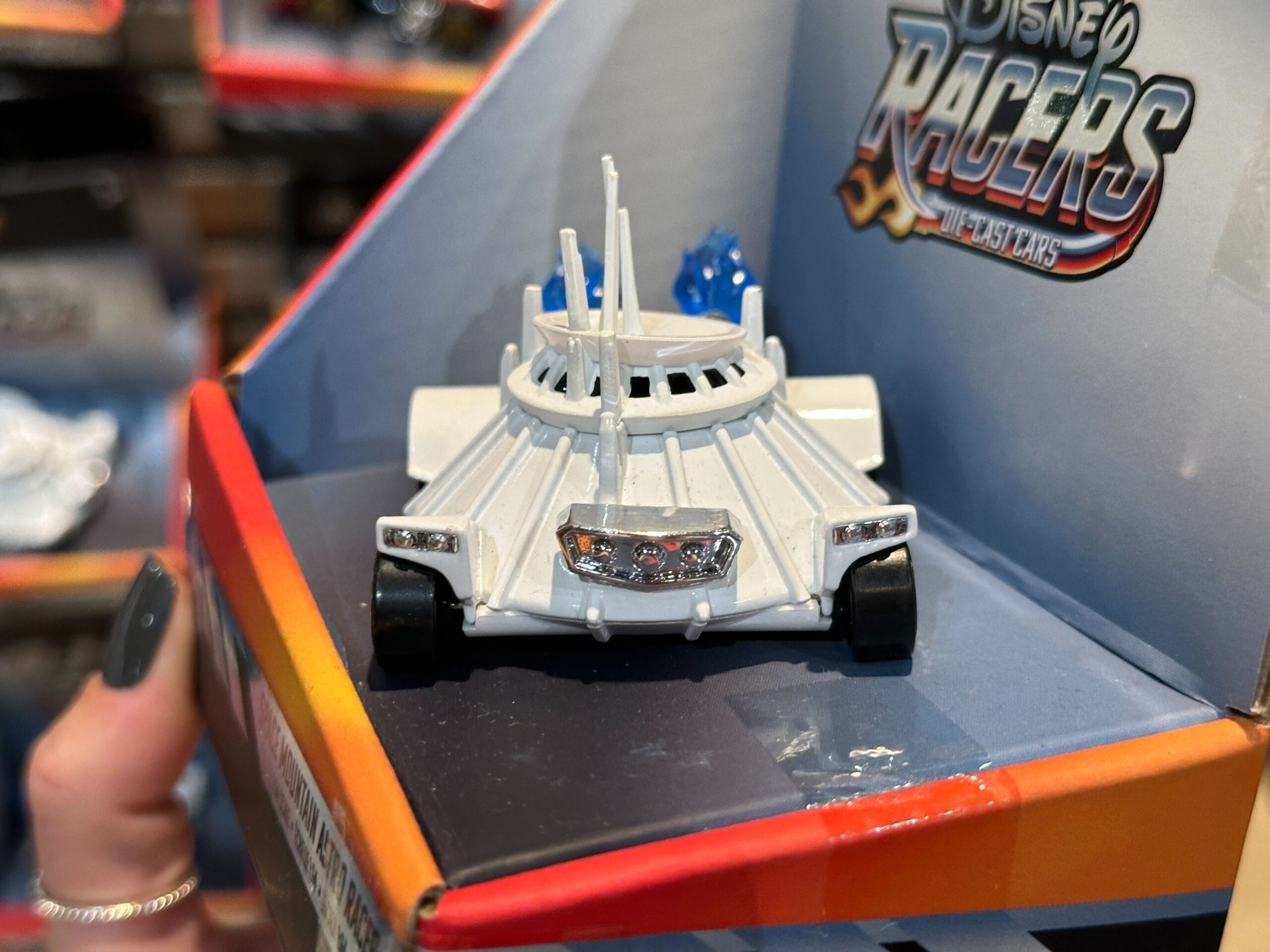 A white Disney Racers toy car with a futuristic design, displayed in its box at Disney World.