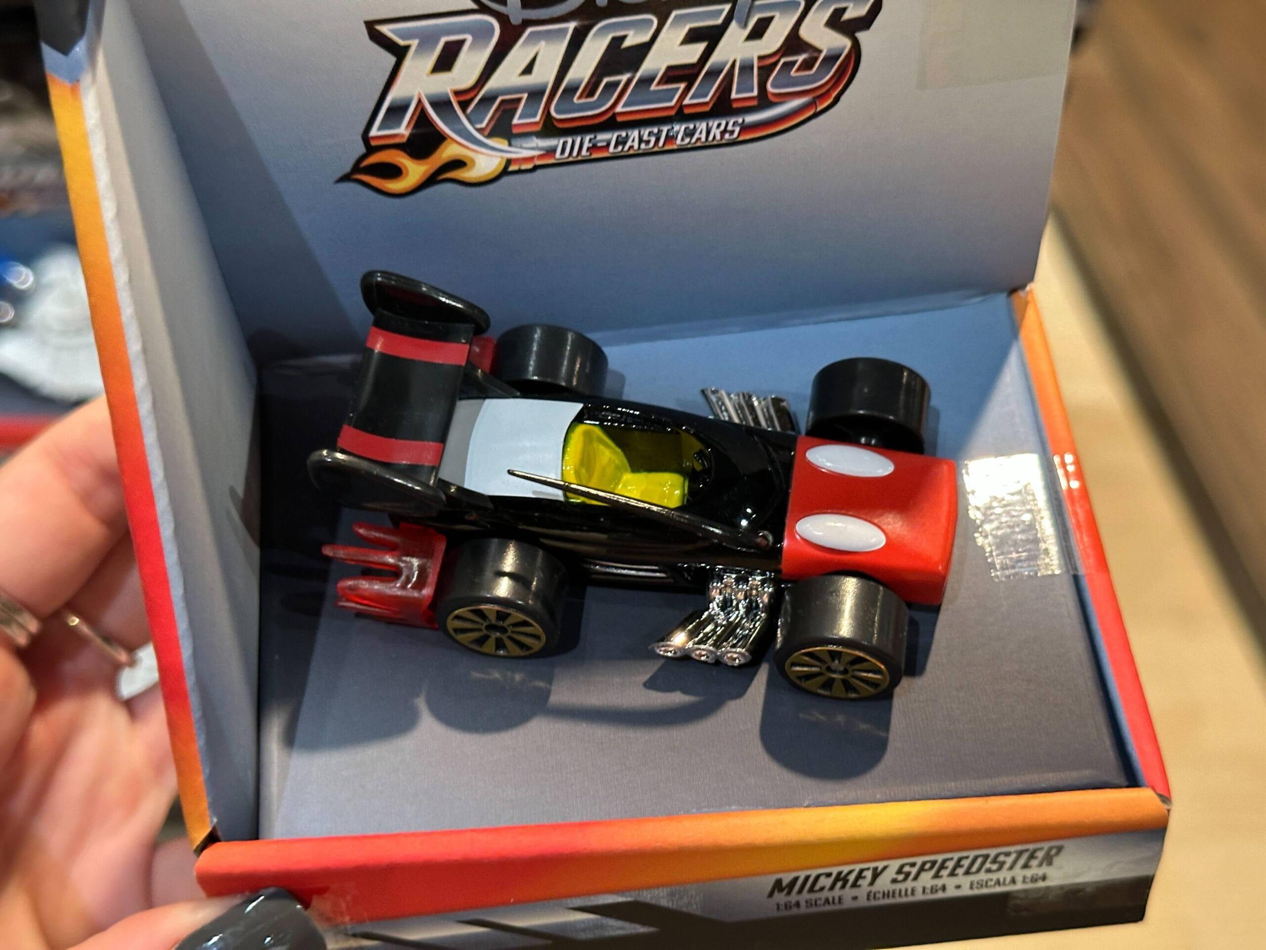 A Disney Racers Toy race car with Mickey Mouse-themed design in a box labeled "Racers Die-Cast Cars.