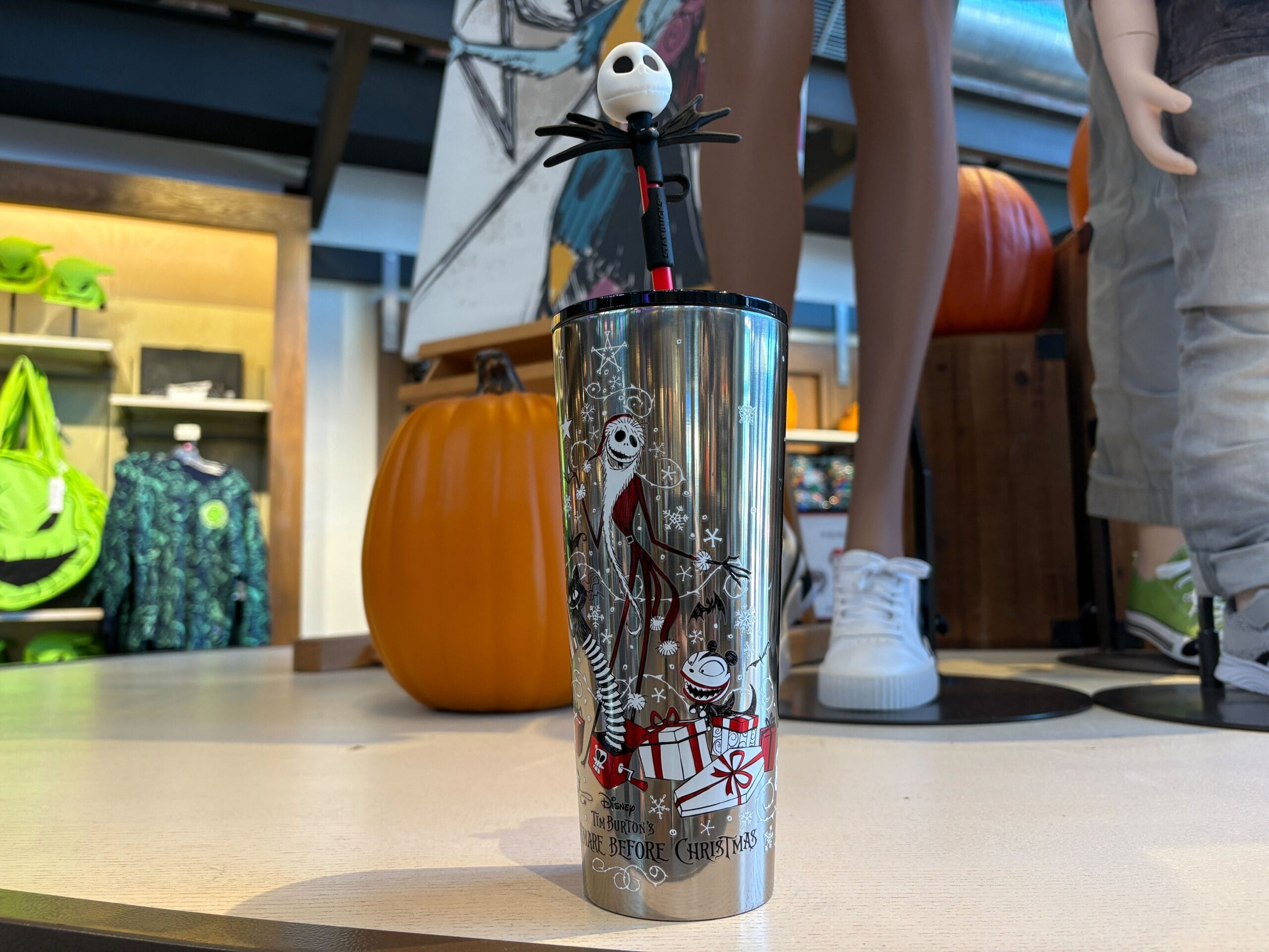 A Nightmare Before Christmas Starbucks Tumbler with Jack Skellington straw, displayed near pumpkins and mannequins.