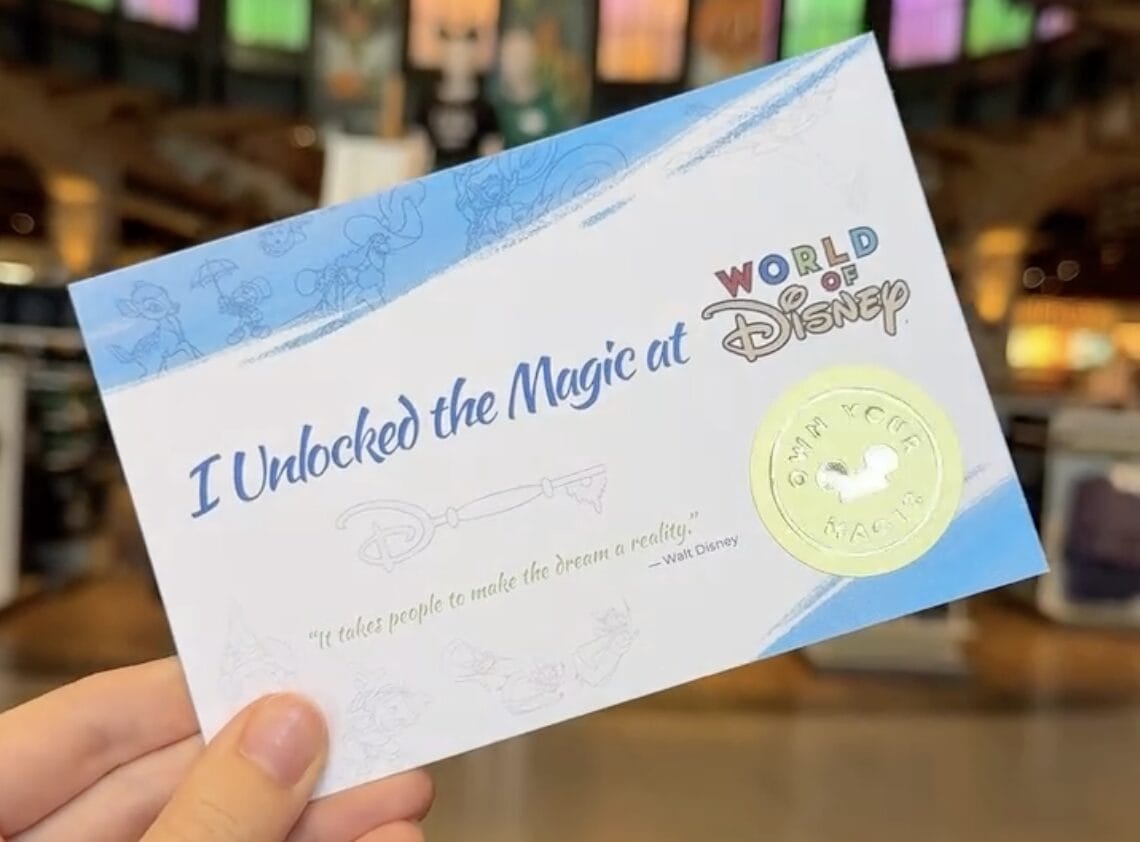 A hand holds a certificate from the World of Disney Opening Ceremony at Disney Springs, featuring a gold seal and magical designs.