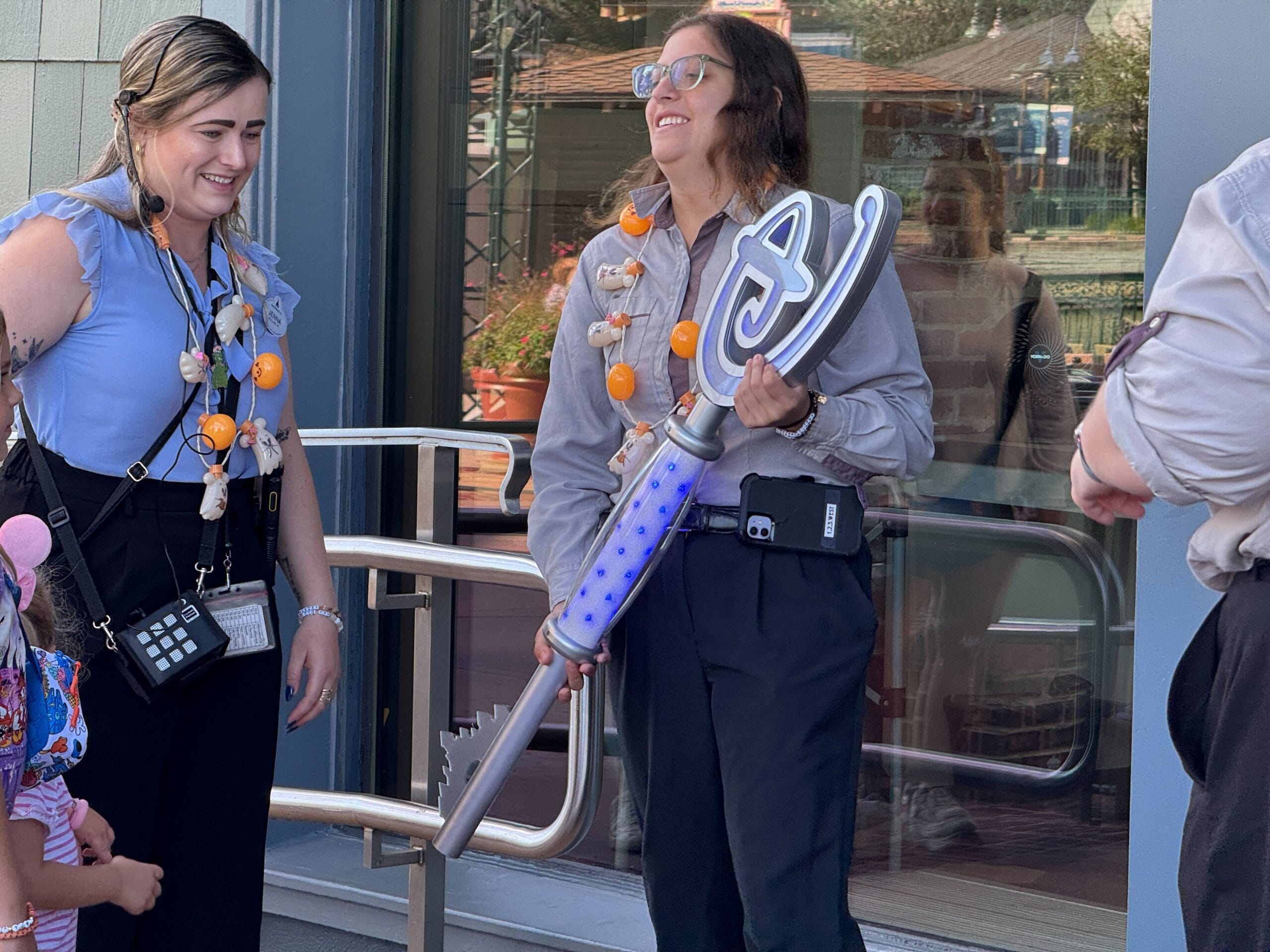 Two women in uniforms smile at the World of Disney Opening Ceremony; one holds a large, silver key with blue lights.