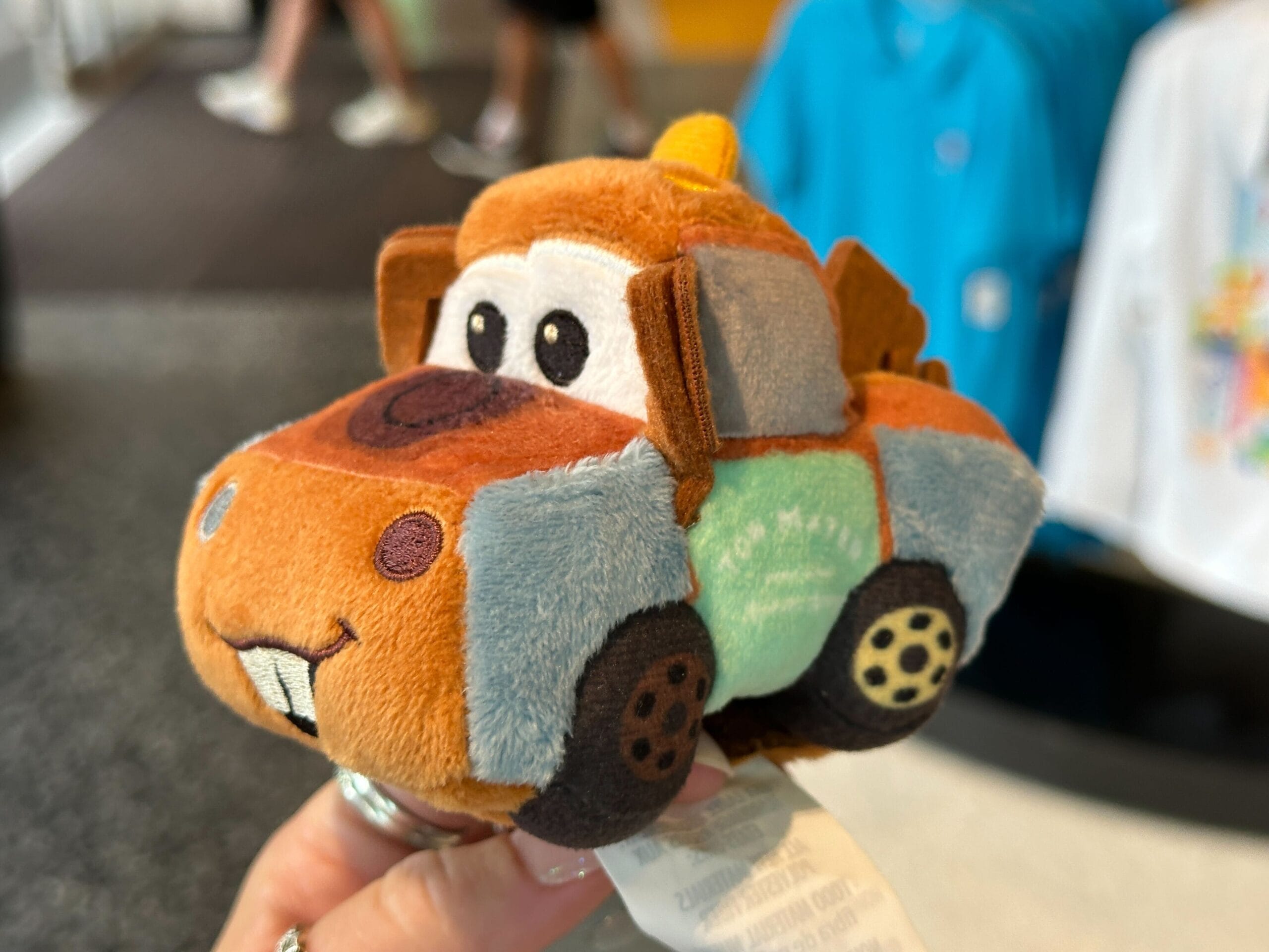A hand holds a Tow Mater plush toy in a store, near Cars Plush Headband options at Disney World.