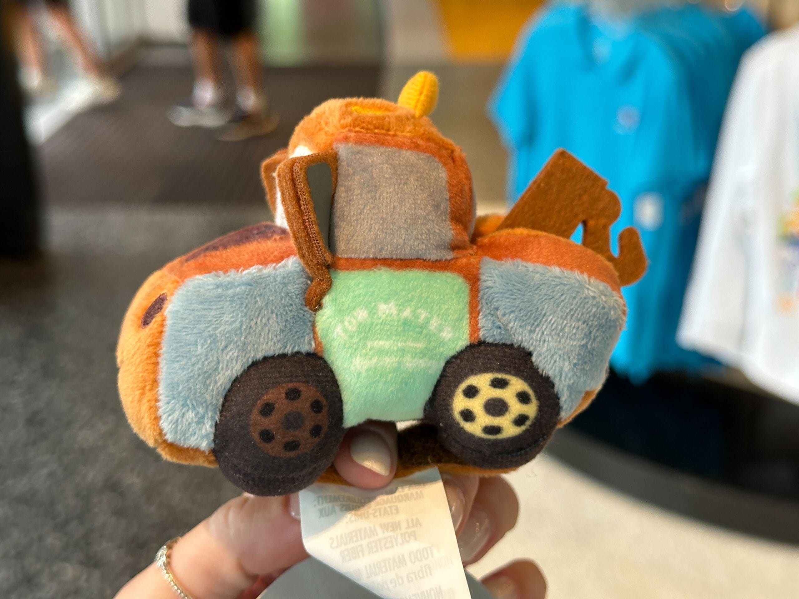 A hand holds a small plush toy tow truck, inspired by Disney World, featuring cartoon-like details.