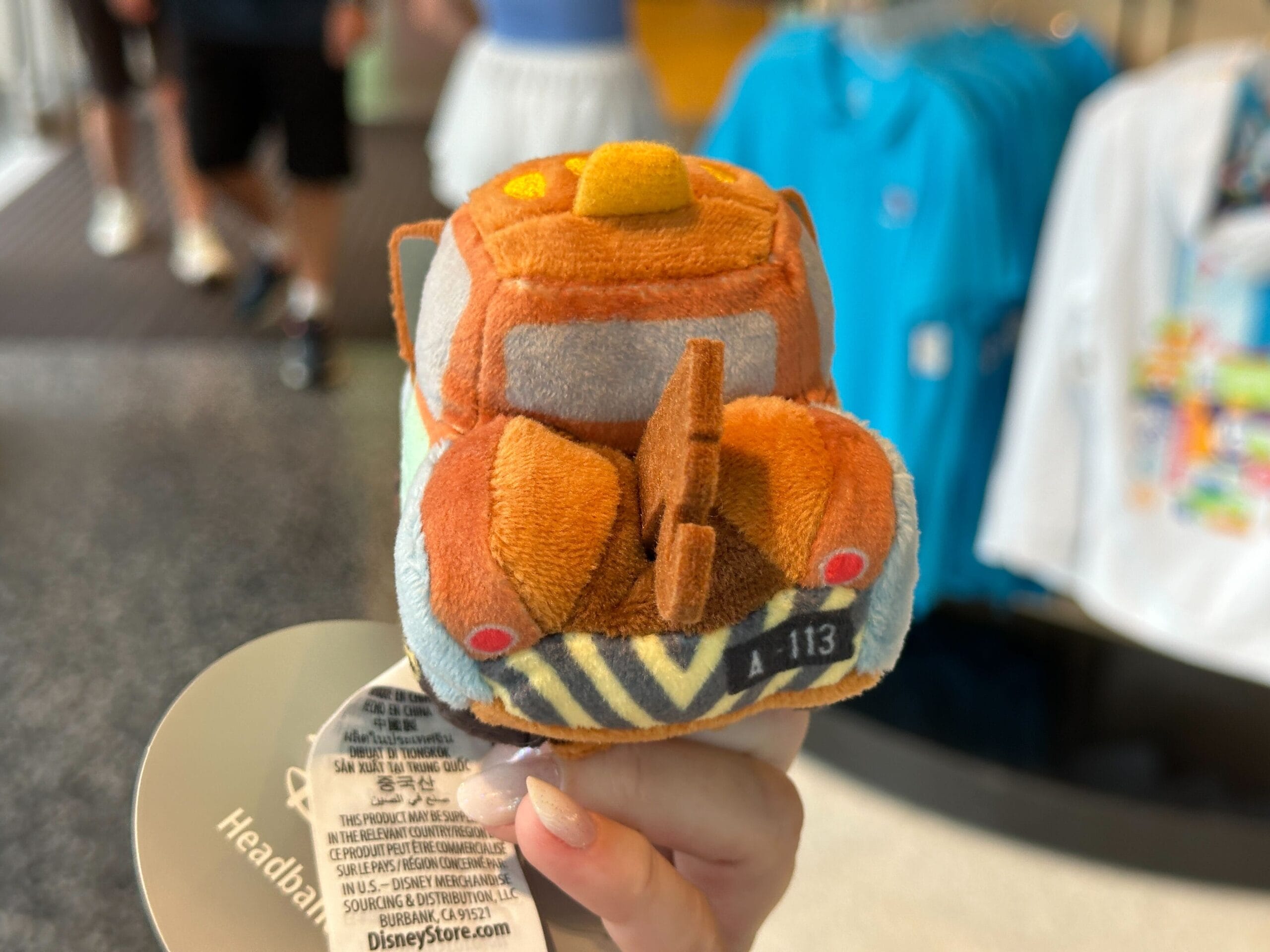 A hand holds a small plush toy of Mater, the Cars character, inside a Disney World store.