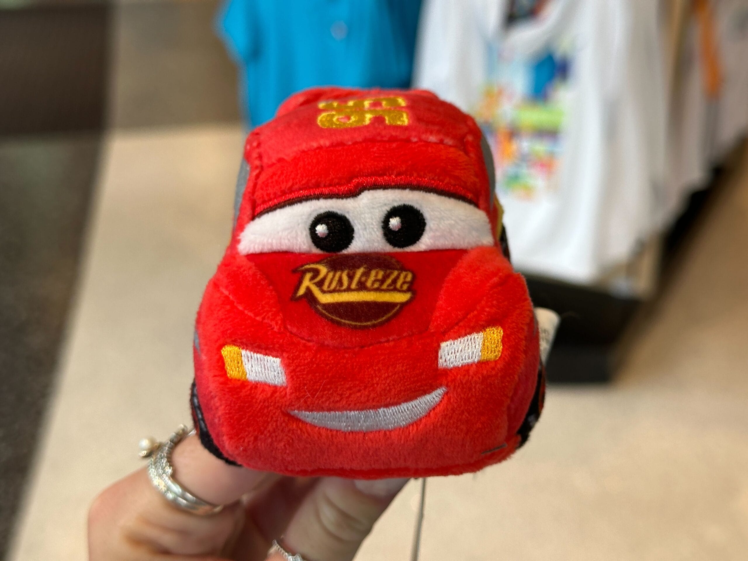 A hand holds a small plush toy of Lightning McQueen from Disney Pixar’s Cars, perfect for a Disney World Cars Plush Headband.