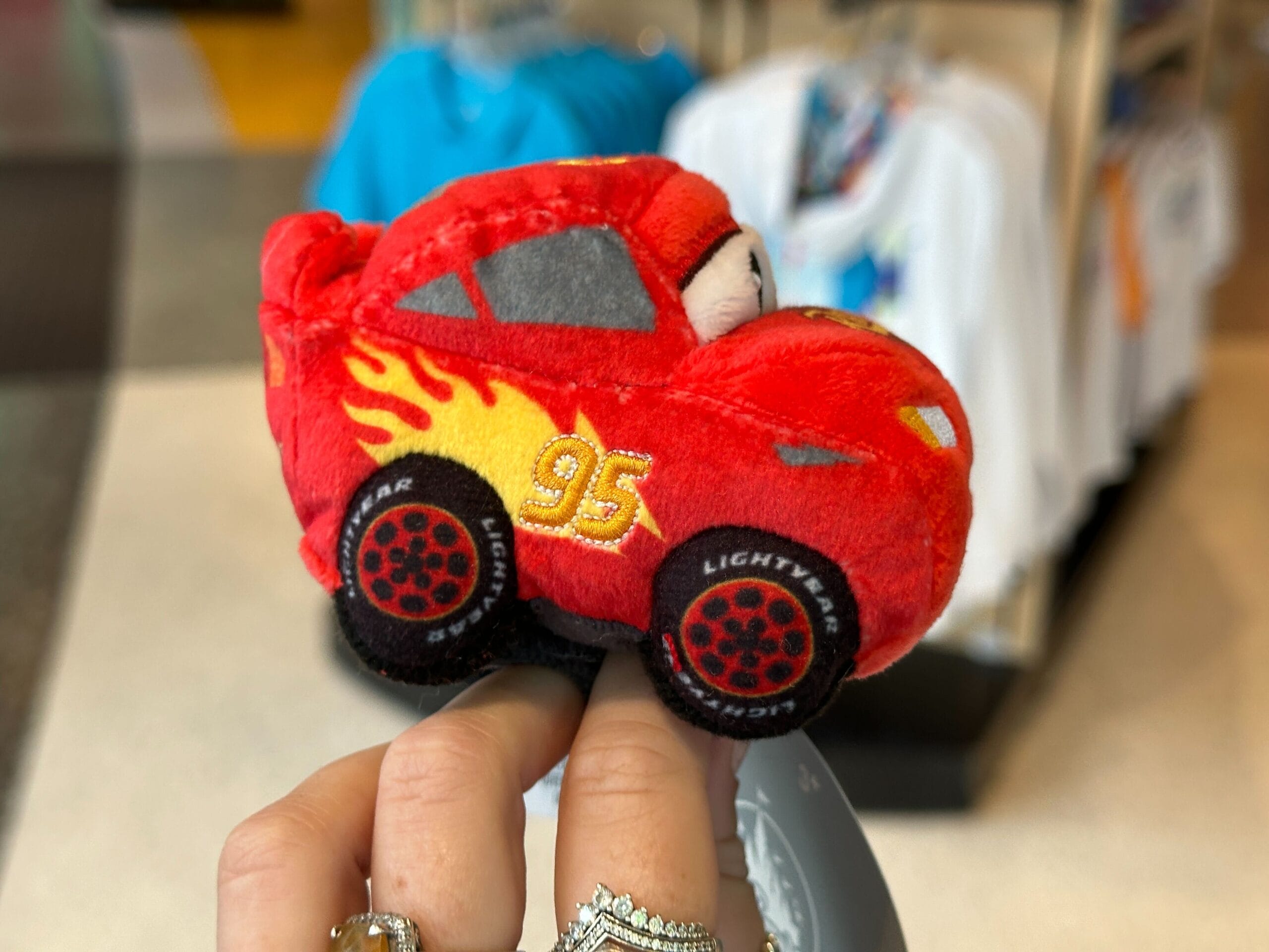 A hand holds a small Lightning McQueen plush toy, perfect for Disney World or pairing with a Cars Plush Headband.